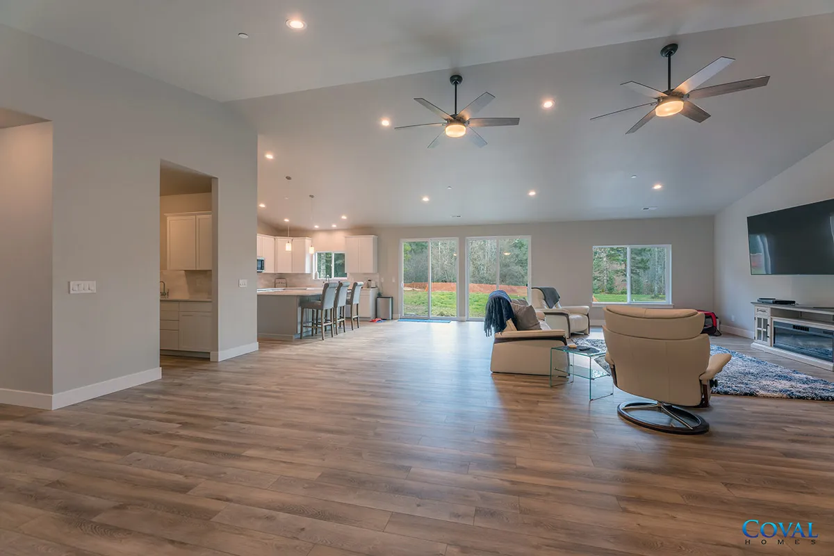 Spacious open-plan living room with wood floors, ceiling fans, and large windows overlooking a patio.