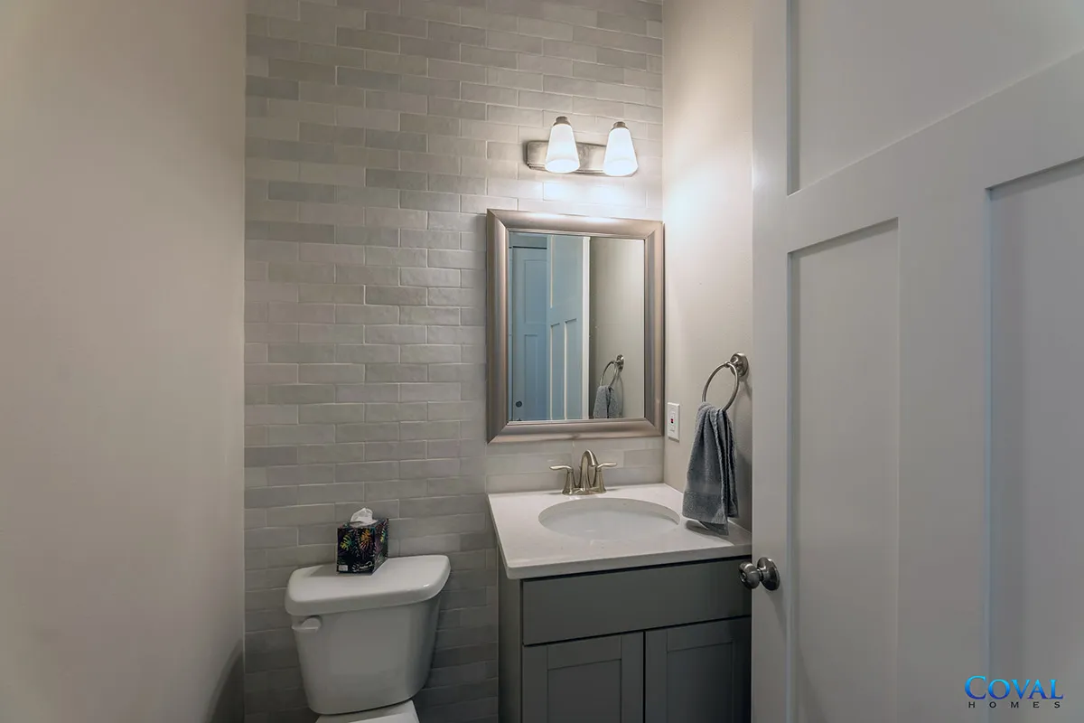 Small bathroom with a toilet, vanity sink, mirror, and wall sconce lights.
