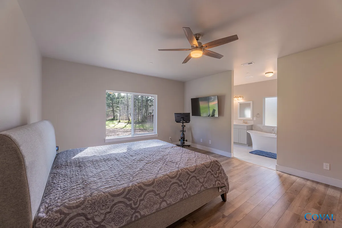 Spacious bedroom with a large bed, ceiling fan, wall TV, and an open view to a bright bathroom.