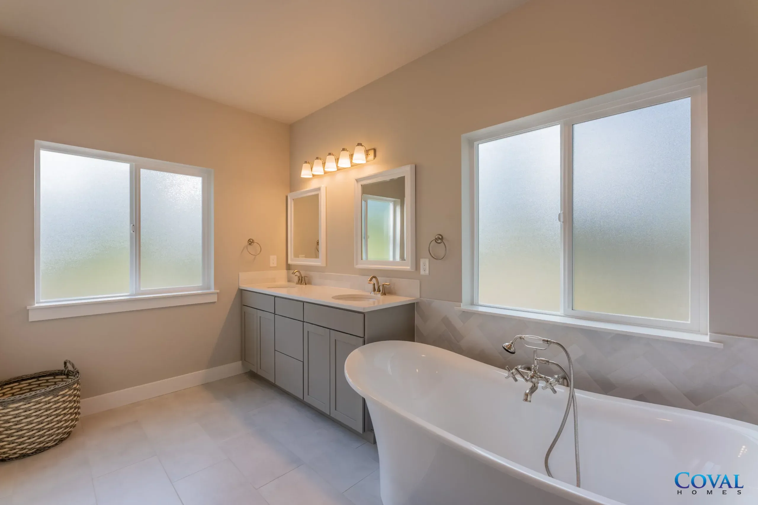 Bright bathroom with frosted windows, double vanity, mirror lights, and a freestanding bathtub.
