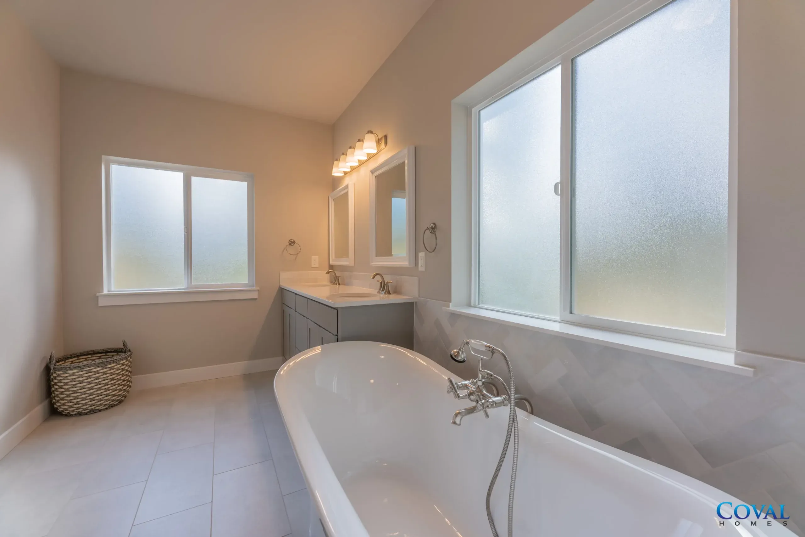 Bright bathroom with a freestanding tub, vanity mirror lights, frosted window, and tiled floor.