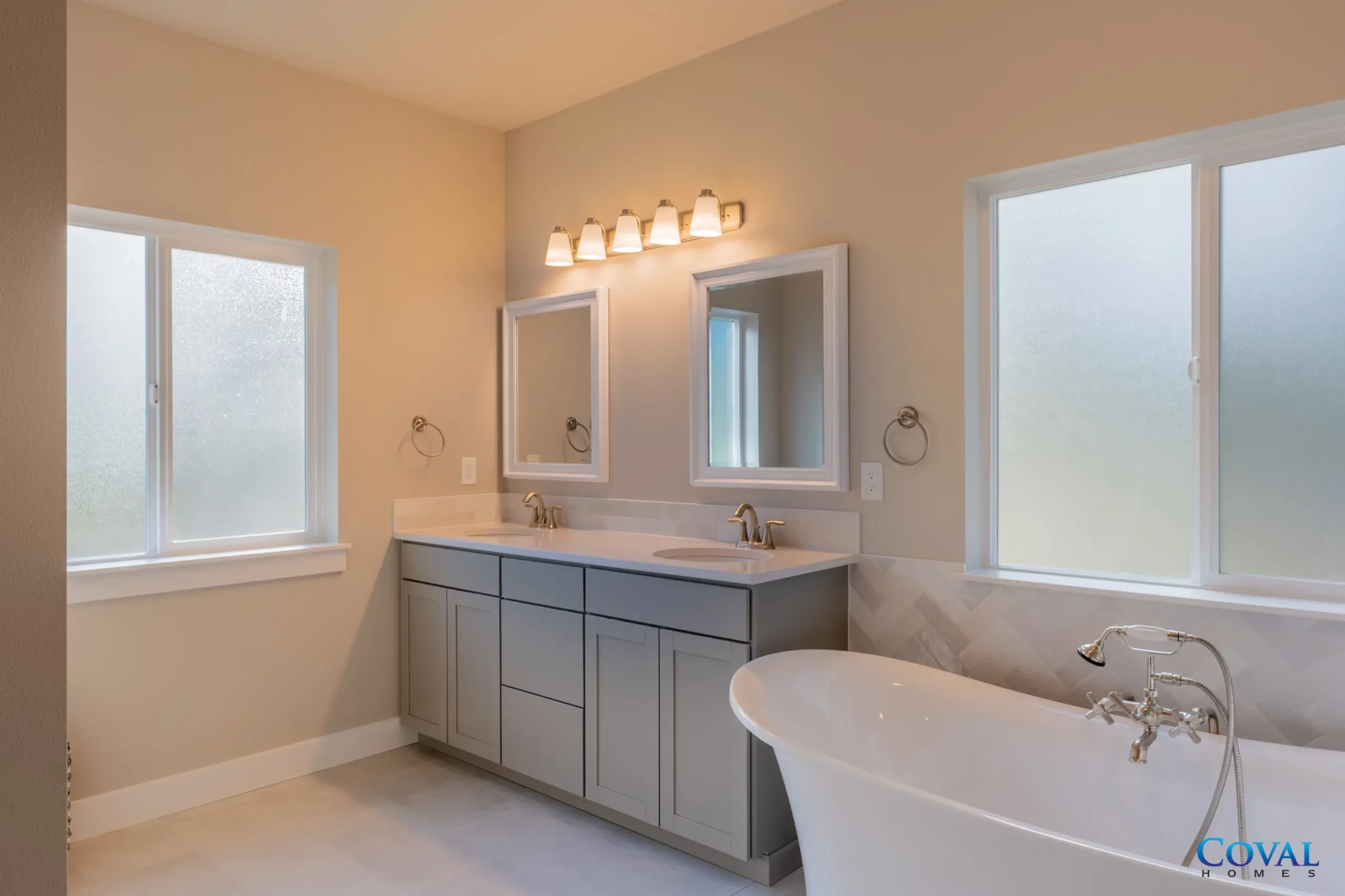 Bright modern bathroom with double vanity, large mirror, frosted windows, and a freestanding bathtub