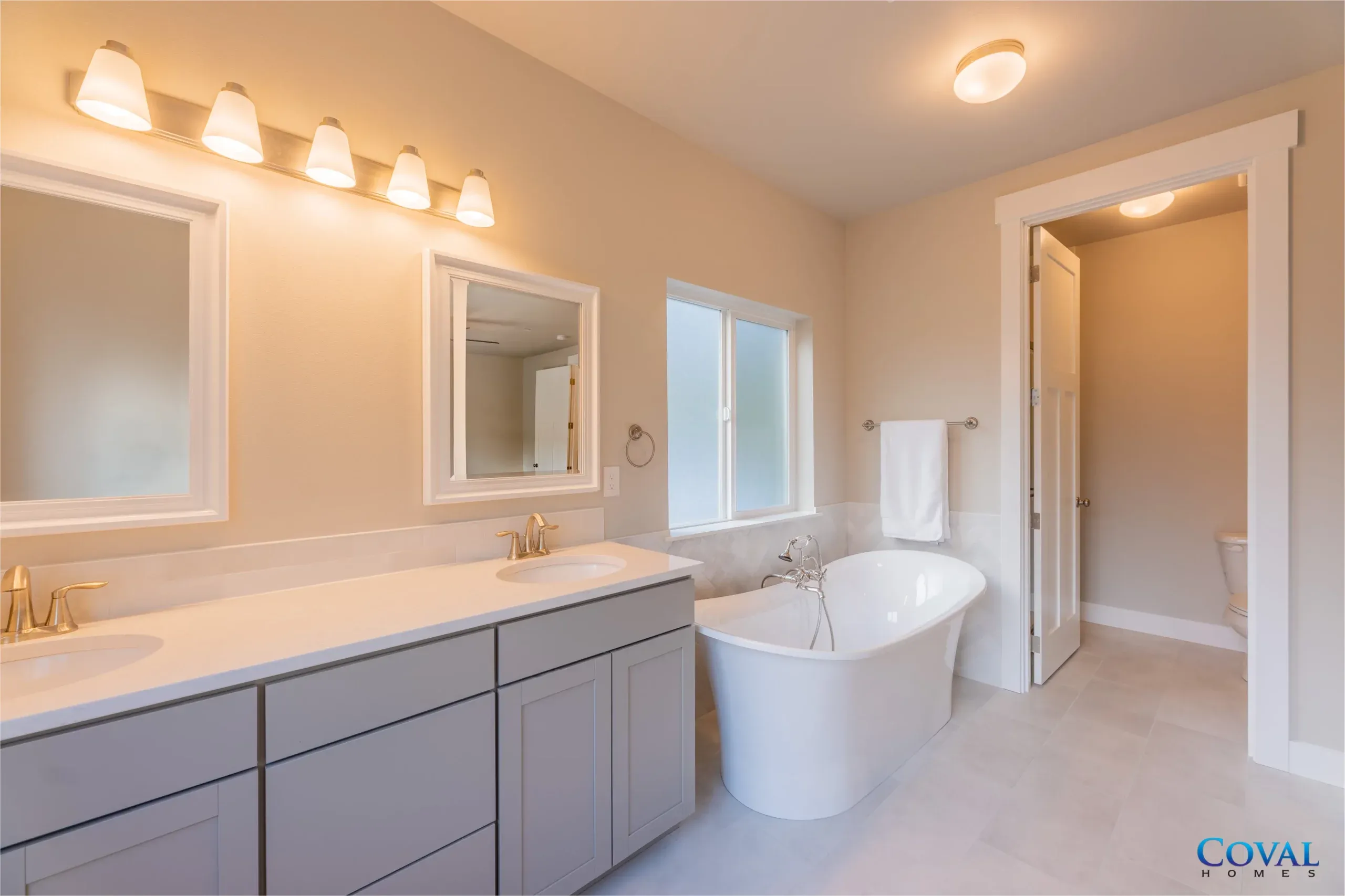 Spacious beige bathroom with double vanity, large mirror, freestanding tub, and open shower doorway