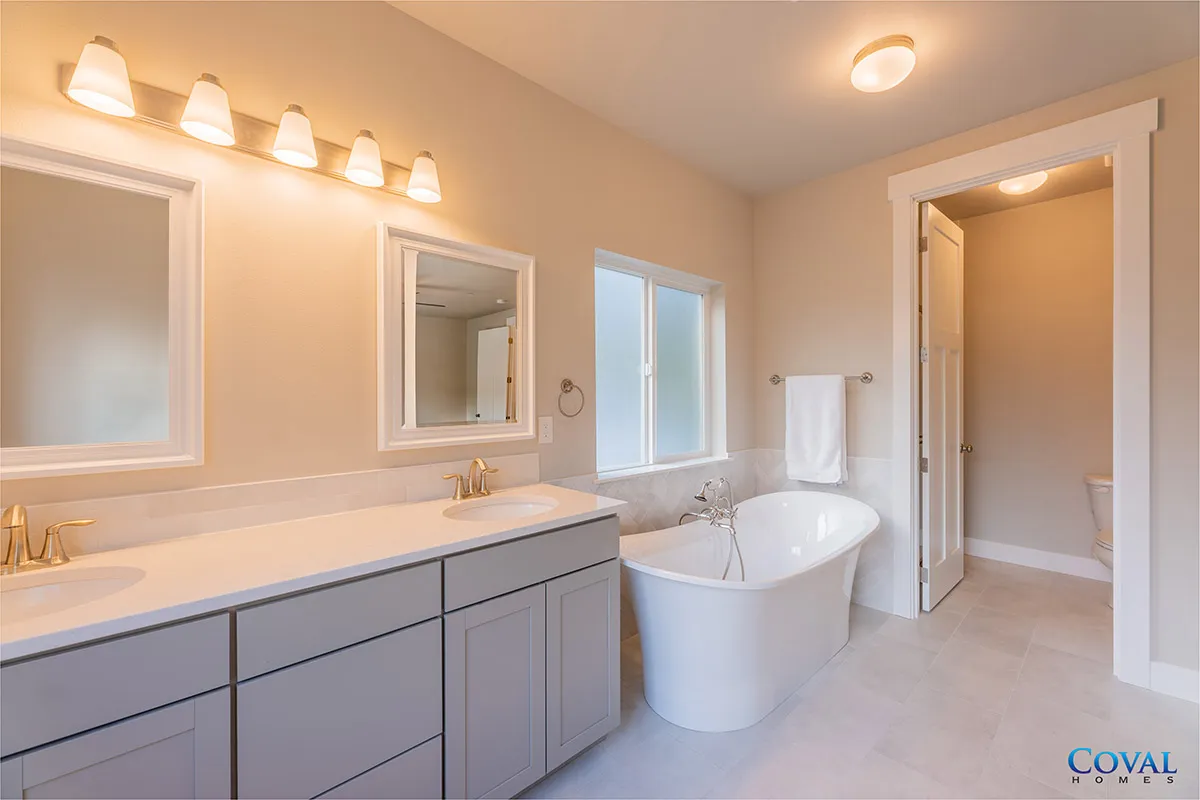 Bright beige bathroom with double vanity, large mirror, freestanding tub, and open shower doorway