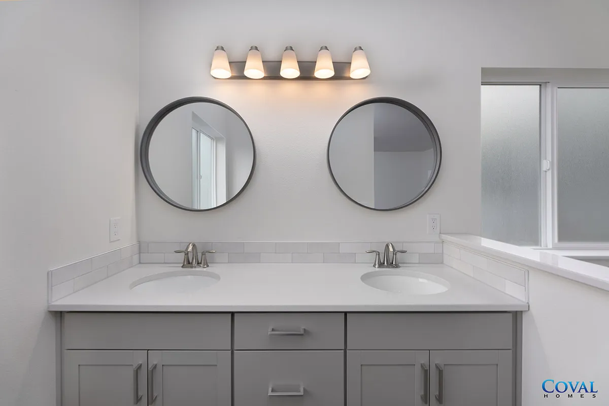 Modern bathroom vanity with double sinks, round mirrors, and wall sconces above a marble countertop