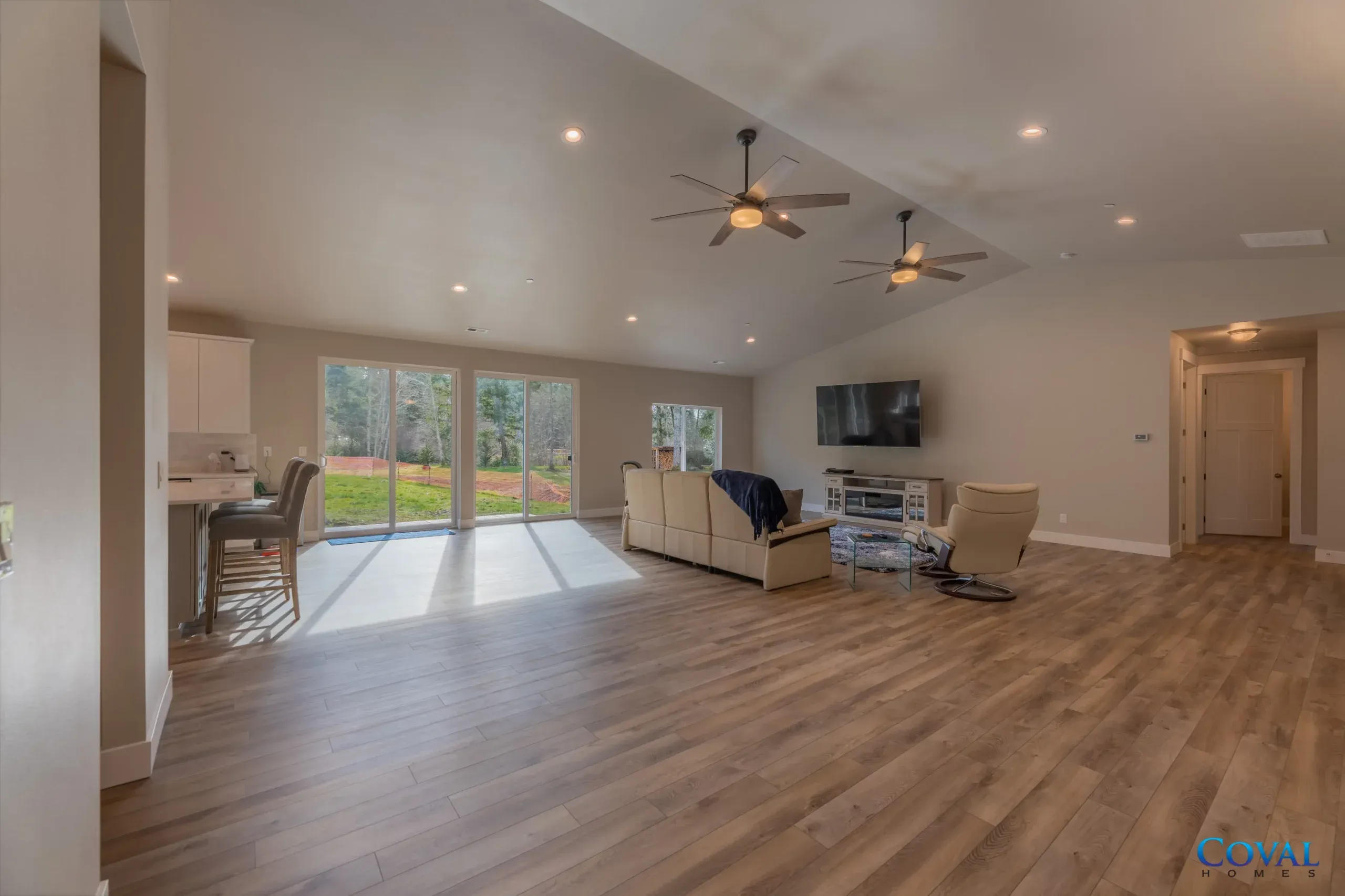 Spacious open-plan living room with wood floors, ceiling fans, sofa, TV, and sliding doors to a backyard