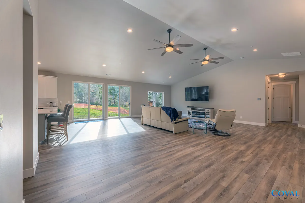 Spacious living room with gray walls, wood floors, ceiling fans, and sliding glass doors to a backyard.