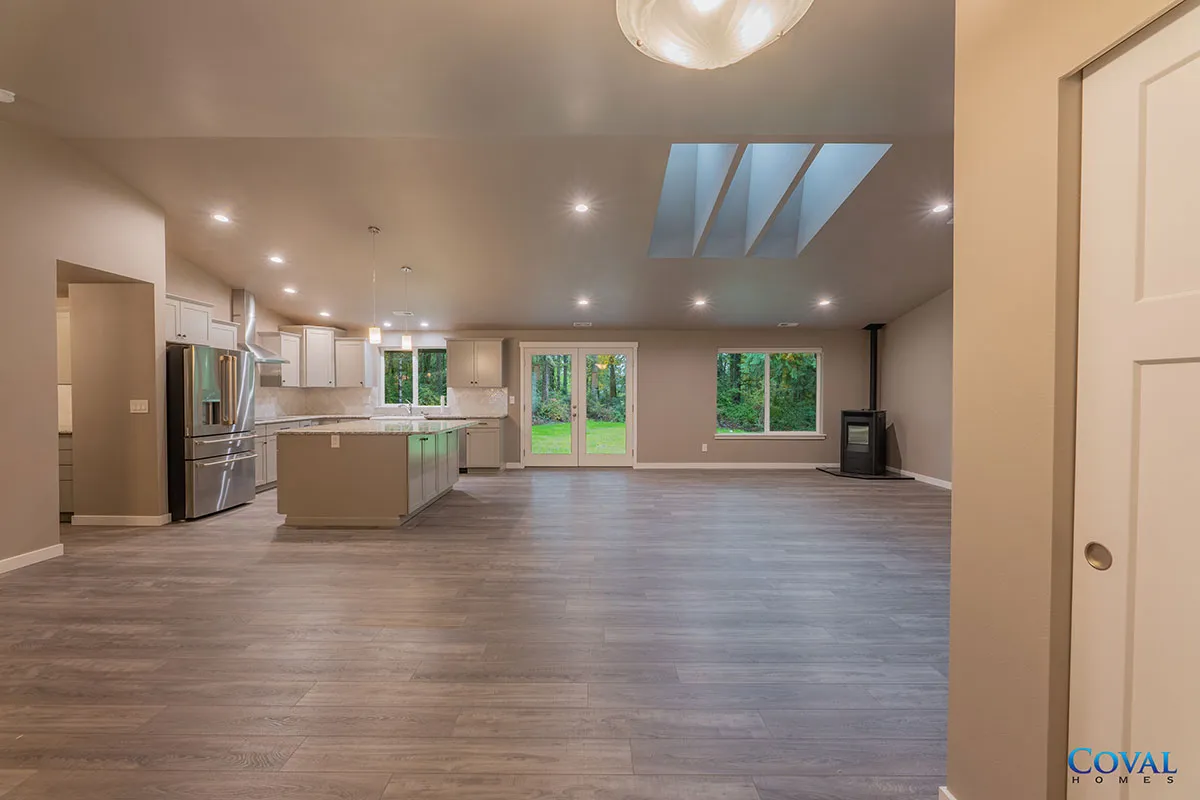 Spacious empty open-plan kitchen and living room with wood floors, island, skylight, and large windows