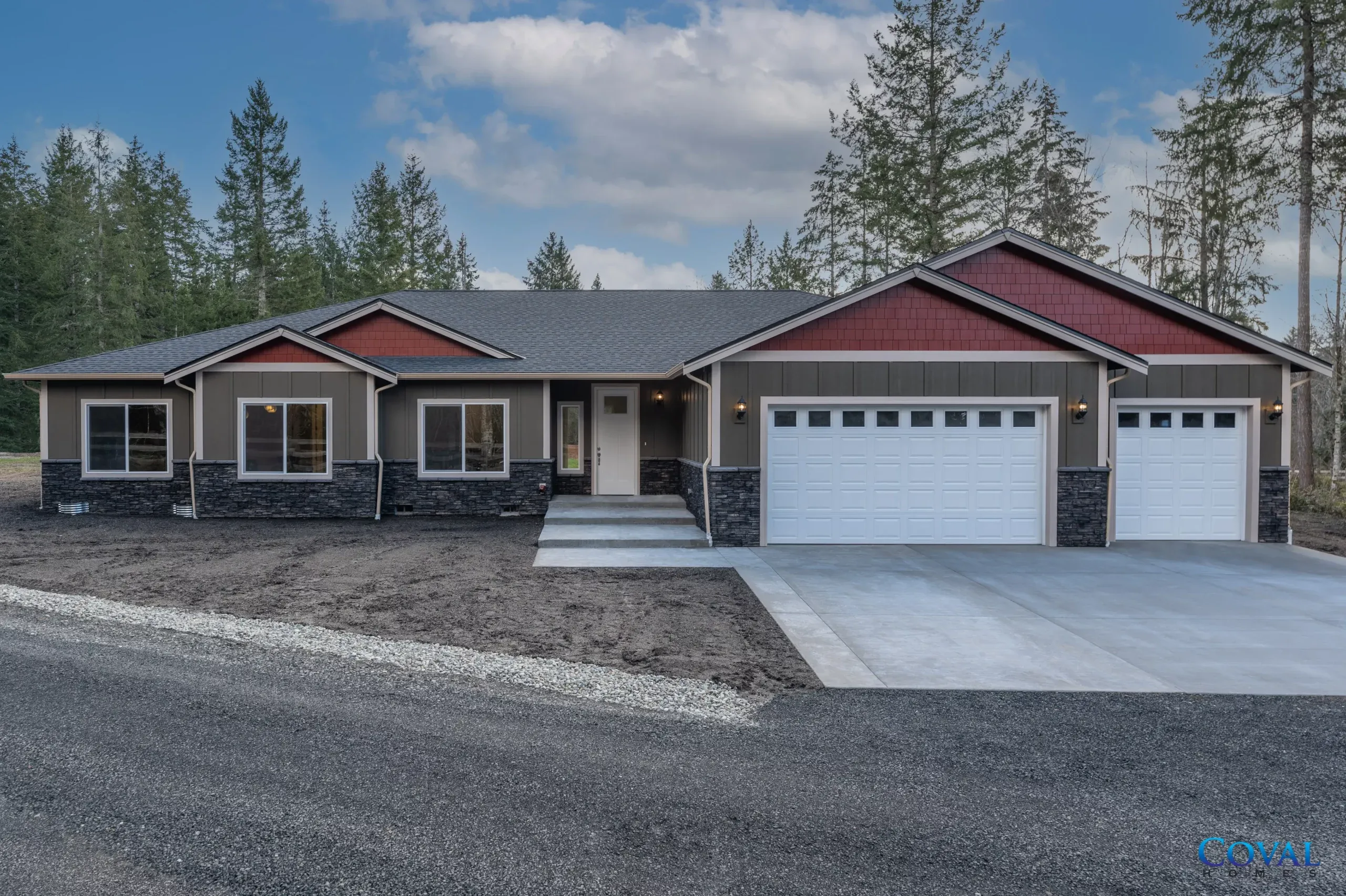 Modern single-story house with a two-car garage and gravel driveway in a wooded setting