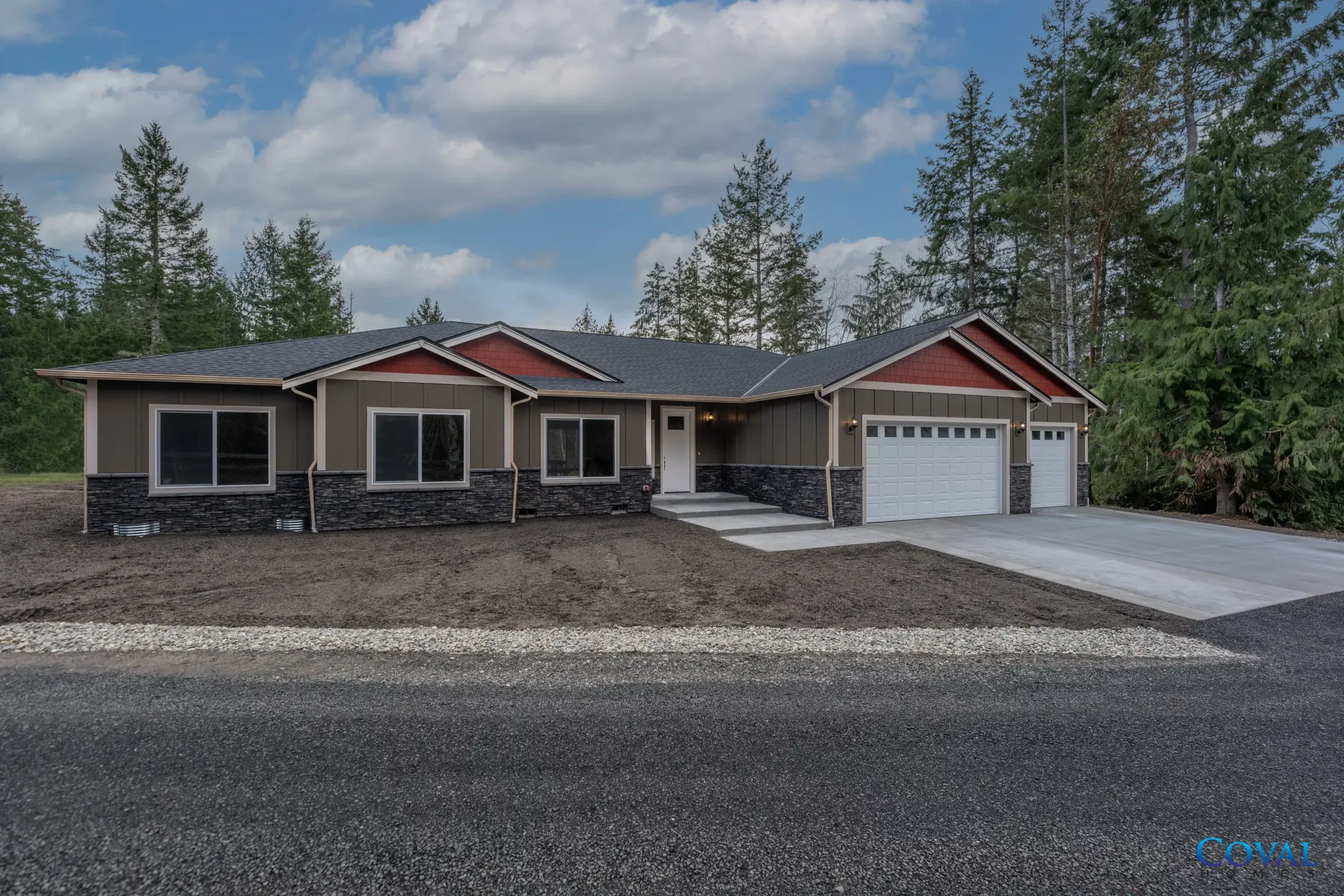 Single-story house with stone facade, red-trimmed roof, and two-car garage on a gravel lot under cloudy sky