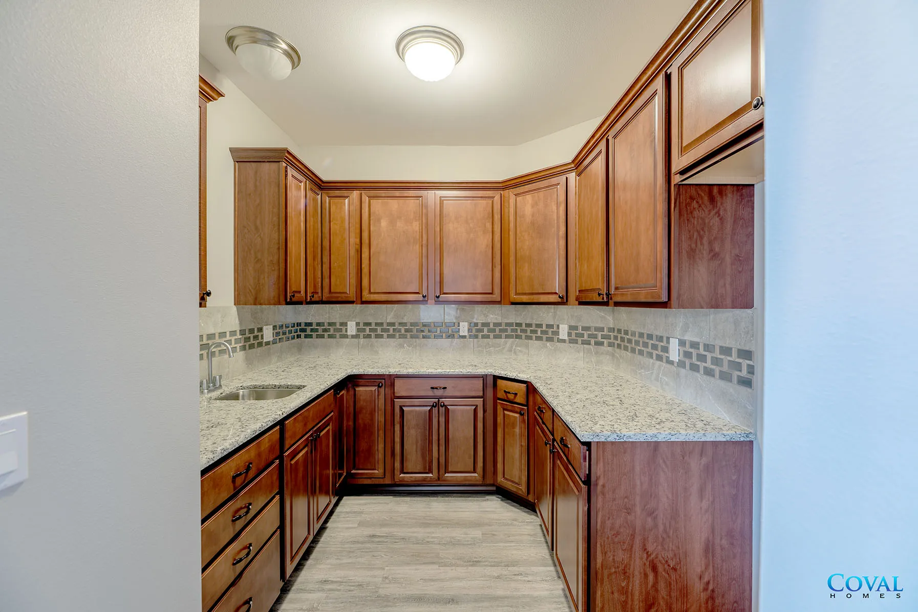 Empty U-shaped kitchen with light wood cabinets, speckled countertops, and tiled backsplash