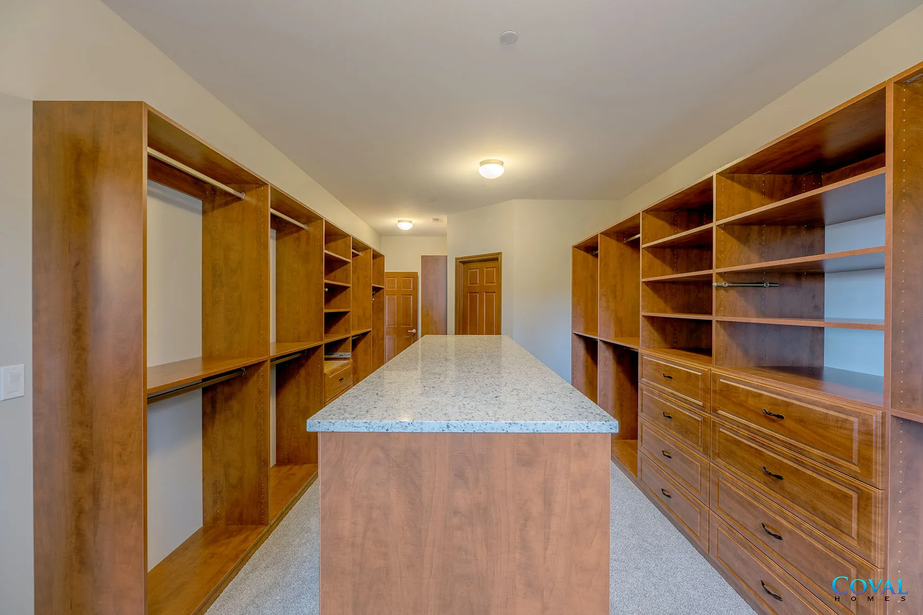 Spacious walk-in closet with wooden shelves and drawers on both sides and a central island counter