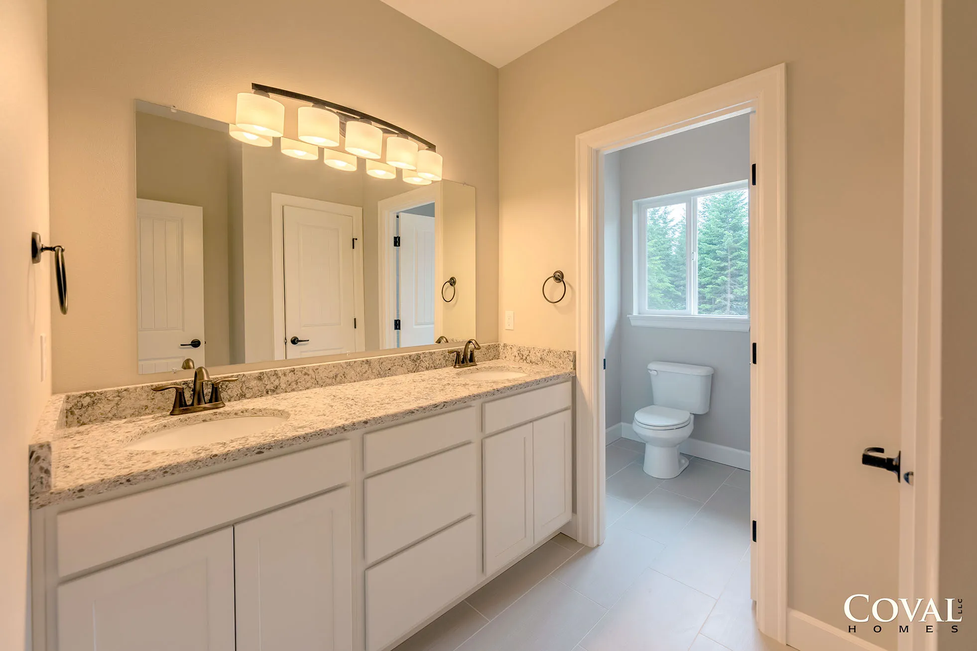 Bright bathroom vanity with granite counter and large mirror, opening to a small toilet room with window.