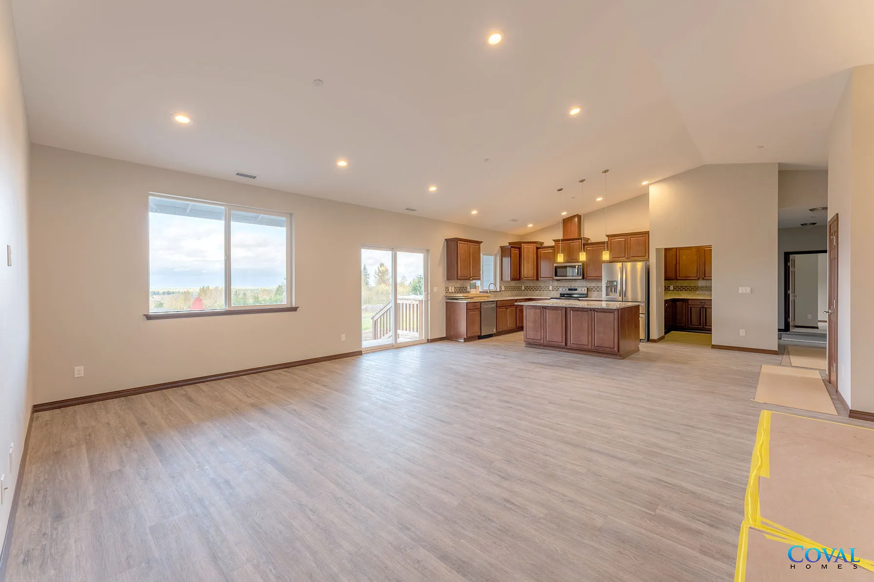 Spacious open-plan living room with kitchen, wood floors, recessed lights, and large windows
