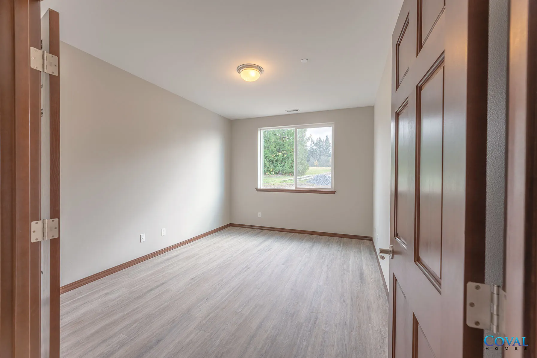 Empty beige room with wood floor, white ceiling light, and a window at the far end