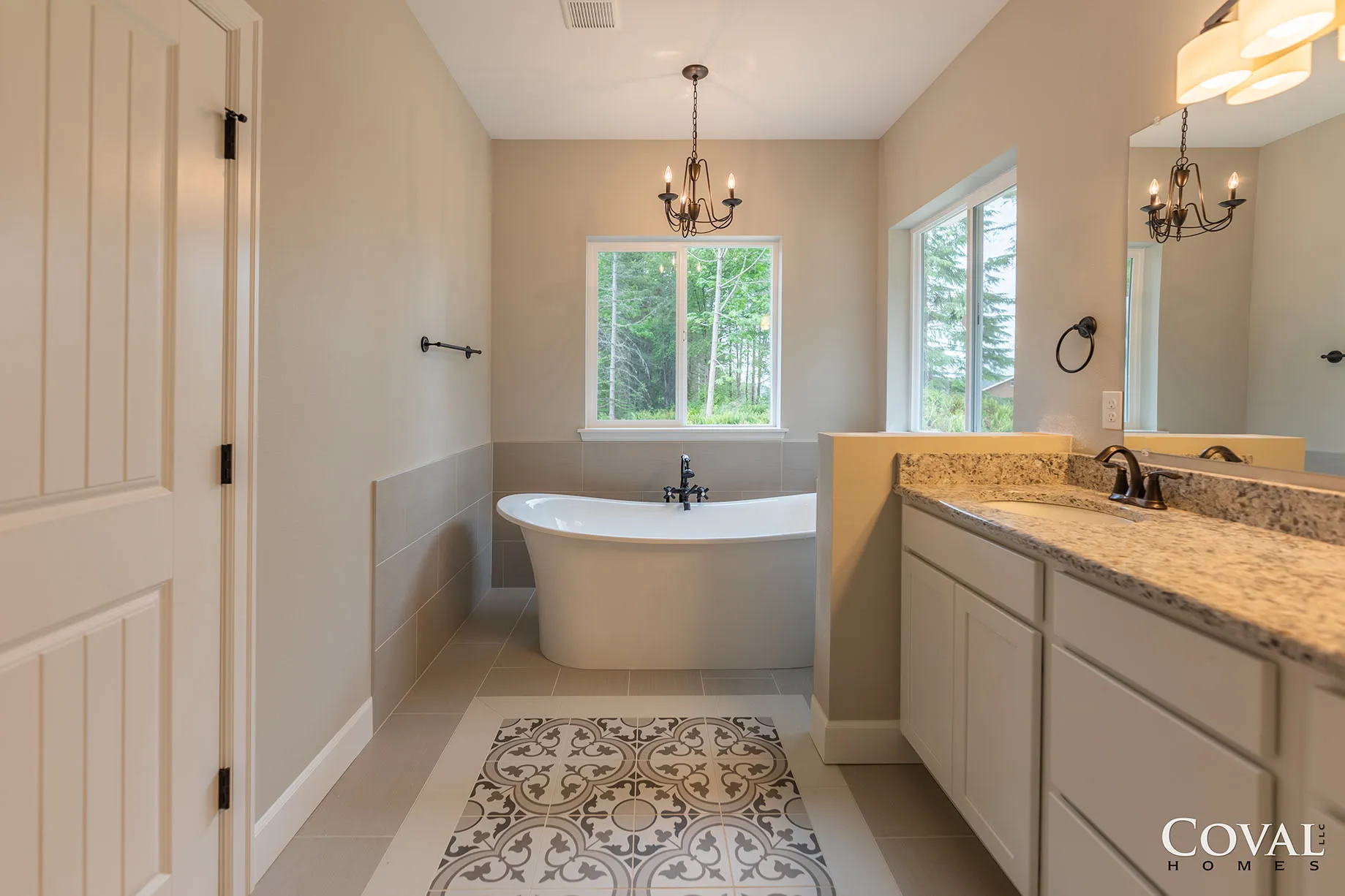 Bright modern bathroom with freestanding tub, double vanity, window, and patterned floor tile.