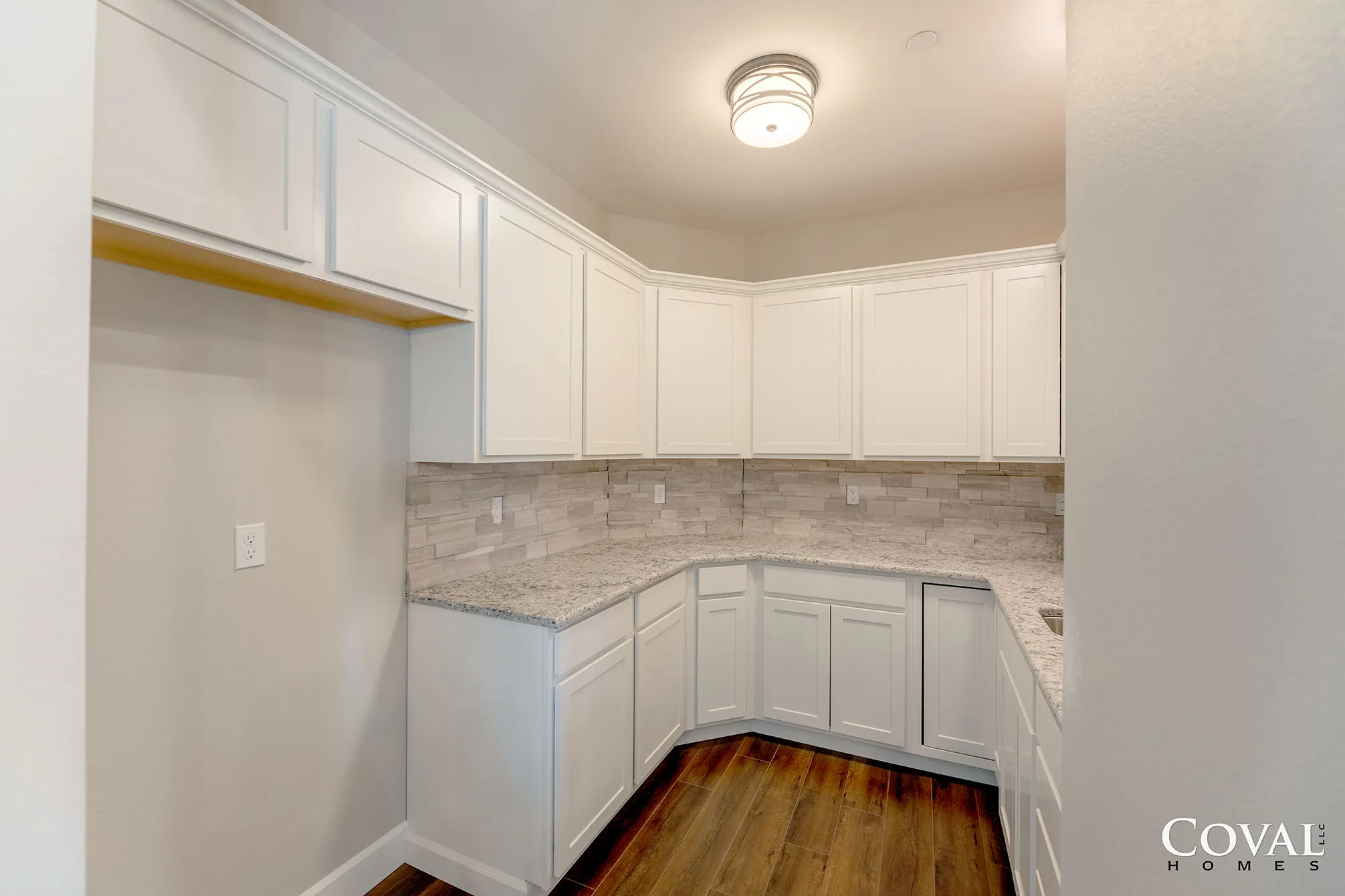 Small white kitchen with curved cabinets, speckled backsplash, and wood flooring