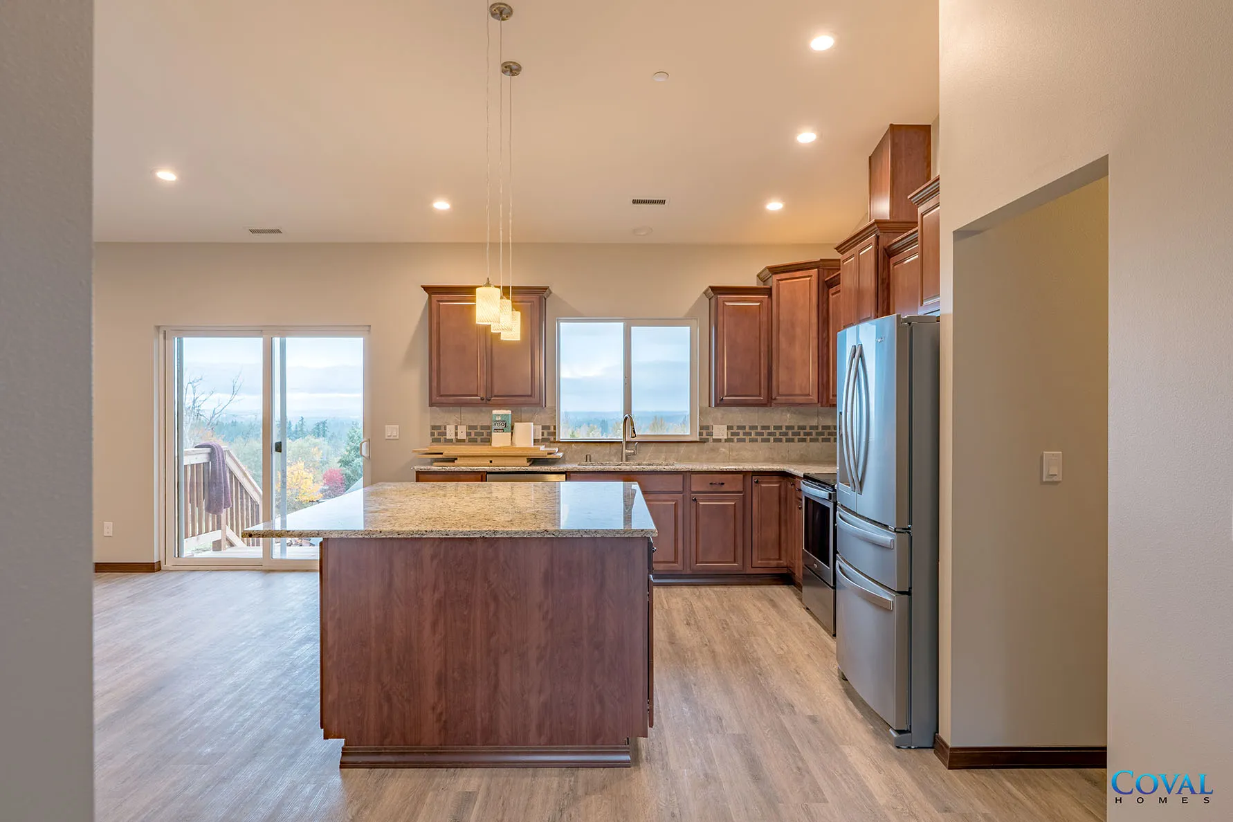 Modern kitchen with wood cabinets, granite island, stainless refrigerator, and sliding glass door to patio