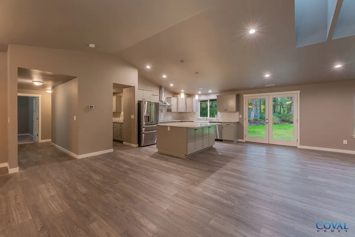 Spacious open-concept kitchen and living area with gray floors, beige walls, and glass doors to a backyard.