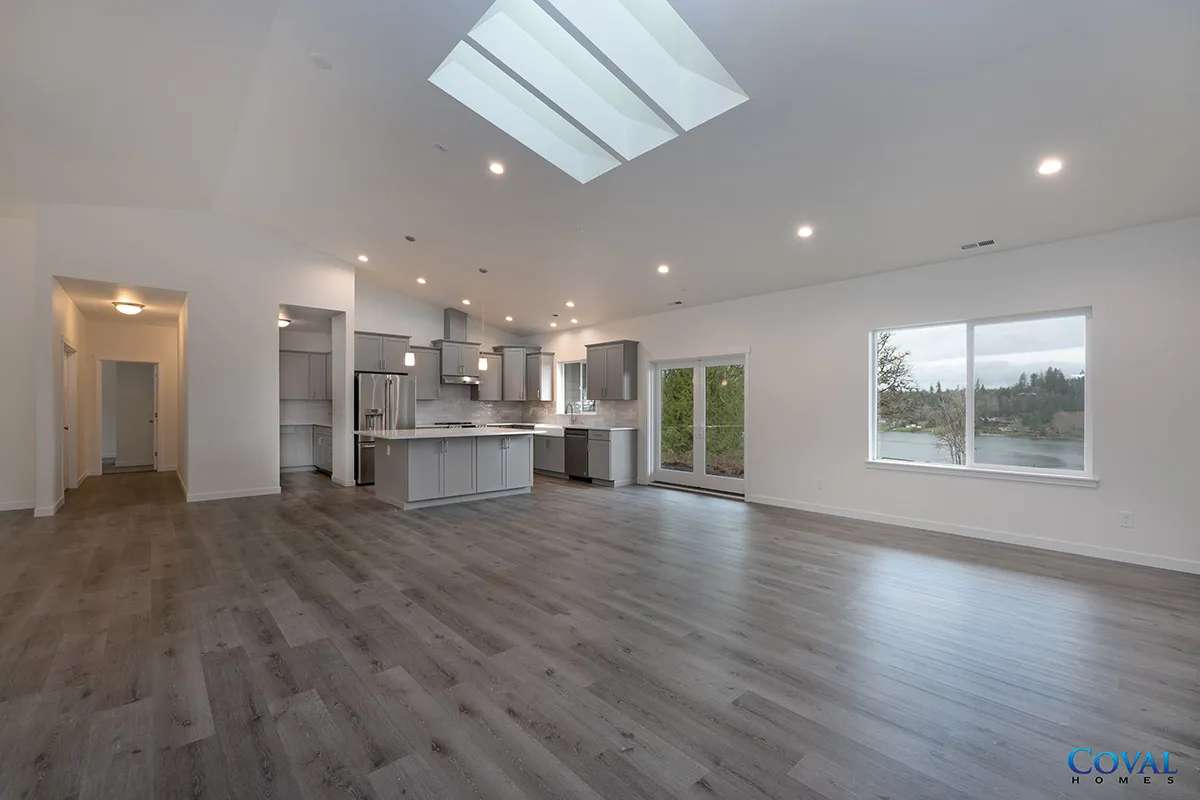Bright open-concept living room with gray wood floors, kitchen island, skylight, and large windows