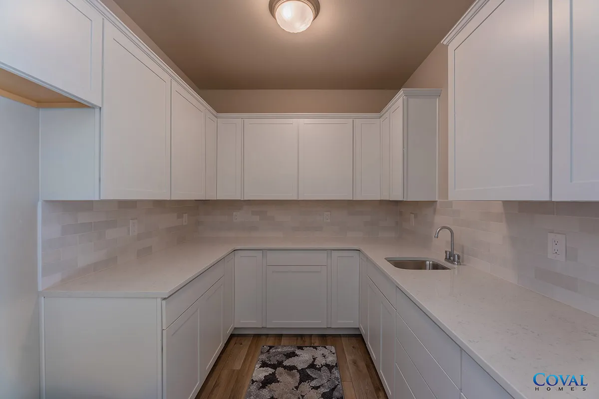 Bright white U-shaped kitchen with upper cabinets, marble counters, wood floor, and ceiling light.
