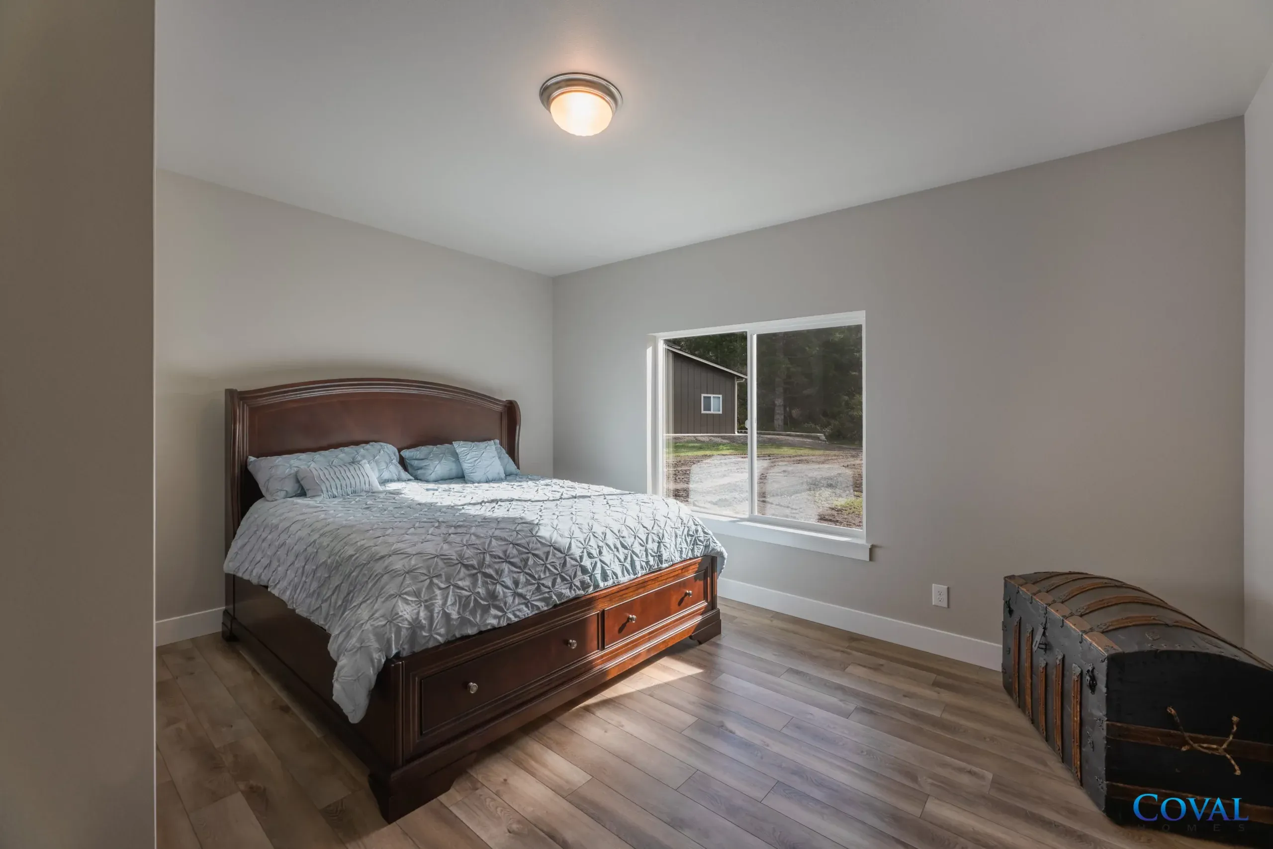 Small bedroom with a dark wooden bed, gray walls, window, and wicker chest.
