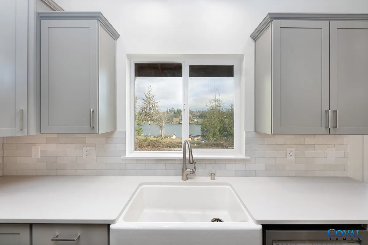 Modern kitchen sink with white countertop, gray cabinets, and a window overlooking a lake.