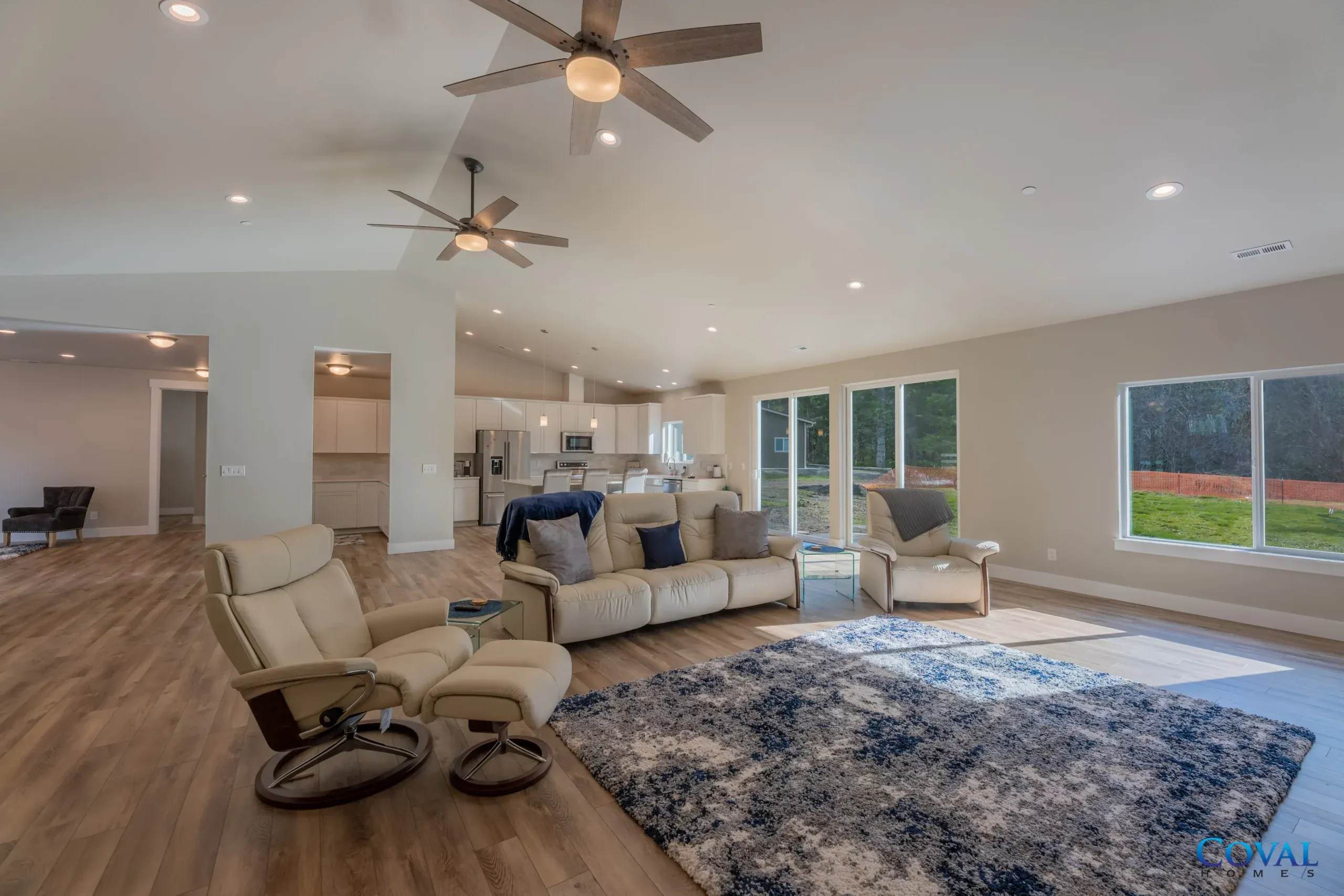 Spacious living room with recliners, sofa, blue rug, ceiling fans, and large windows overlooking a yard