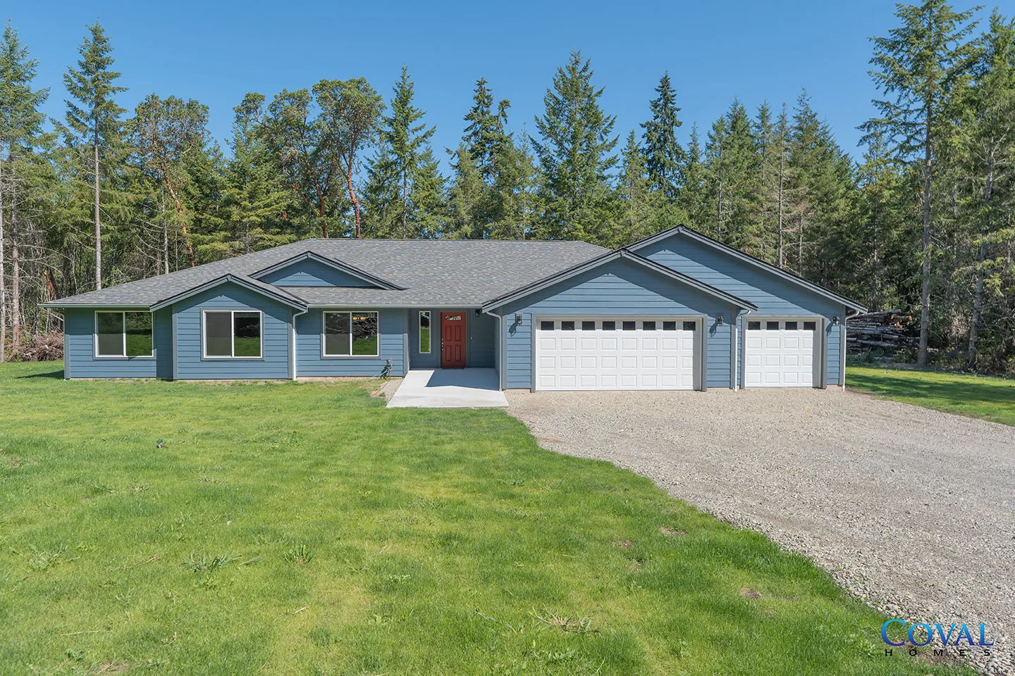 Single-story blue house with three-car garage, gravel driveway, and green lawn bordered by trees.