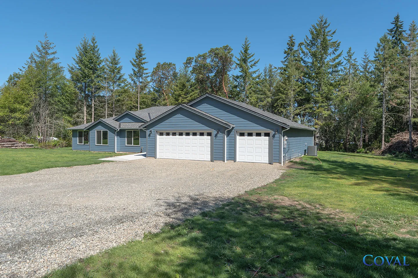 Single-story blue house with three garage doors, gravel driveway, and tall trees in the background