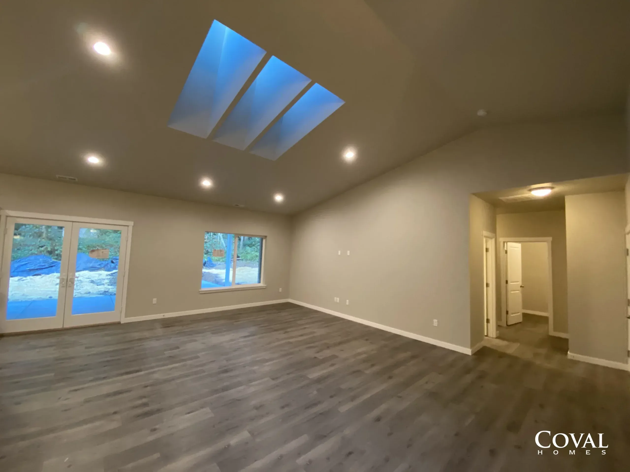 Empty modern living room with skylight, dark wood floors, beige walls, and windows overlooking trees