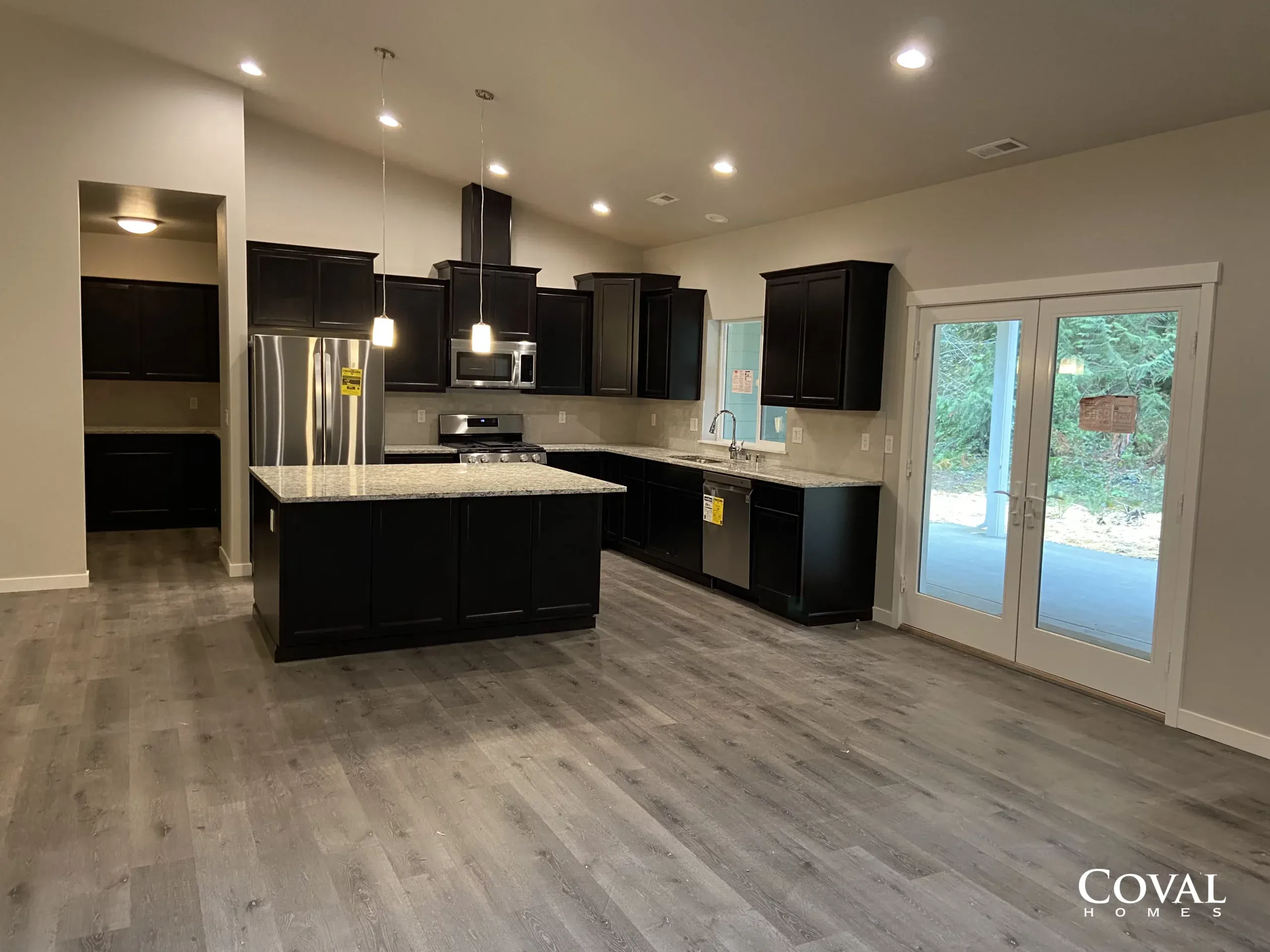 Empty modern kitchen with black cabinets, stainless appliances, island, and French doors to a wooded yard