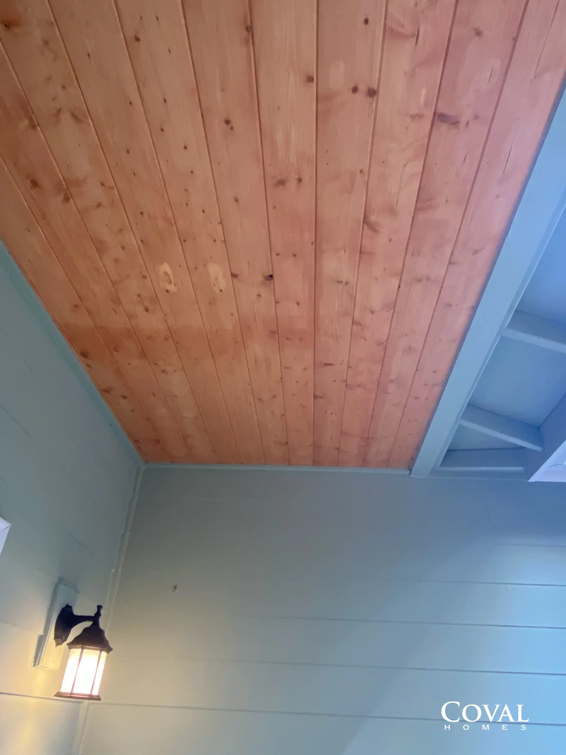 Wood-paneled ceiling above a pale green wall with a lit lantern-style wall sconce.