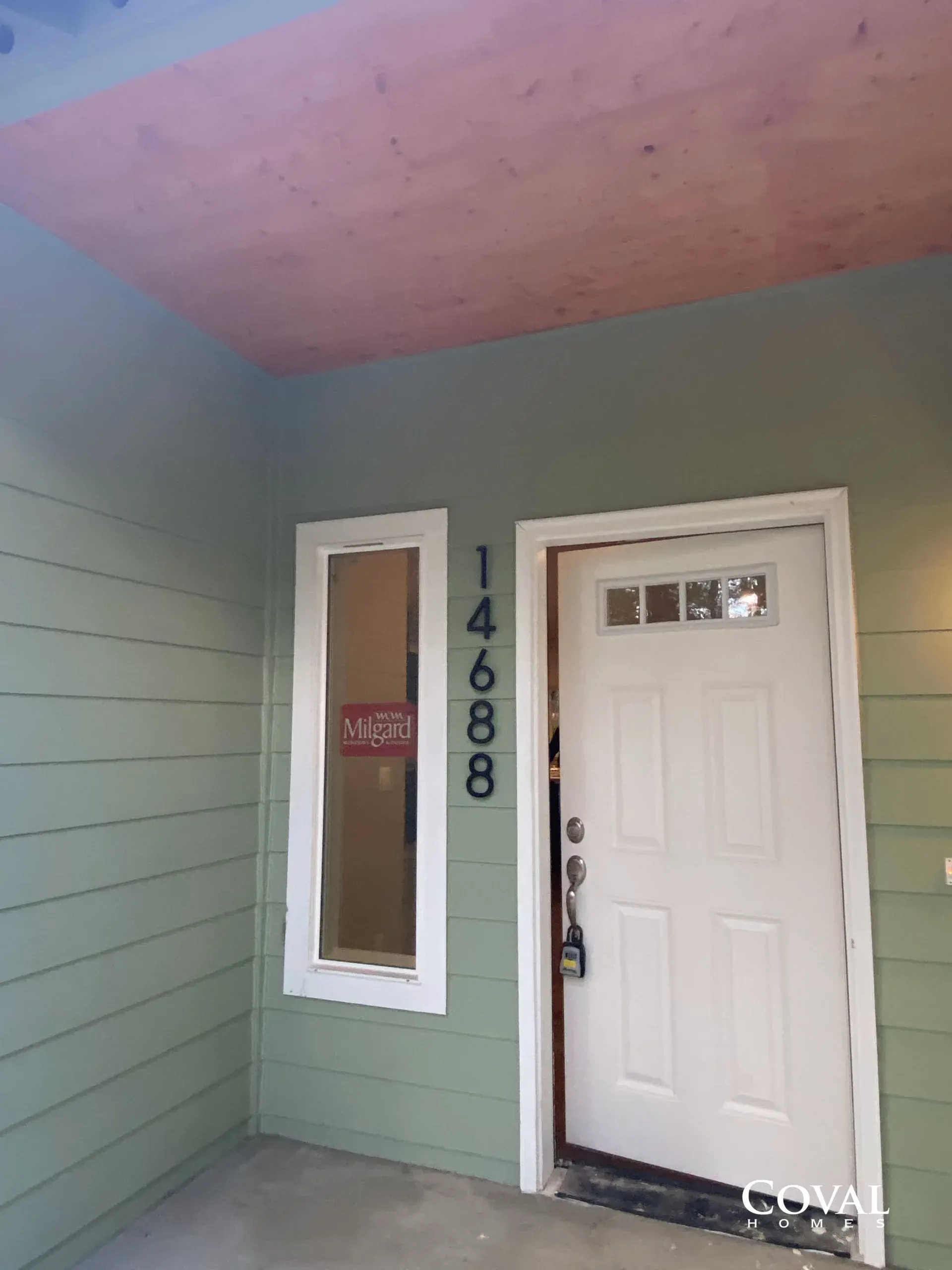 Front porch with white door, green siding, narrow window, and house number 14688.