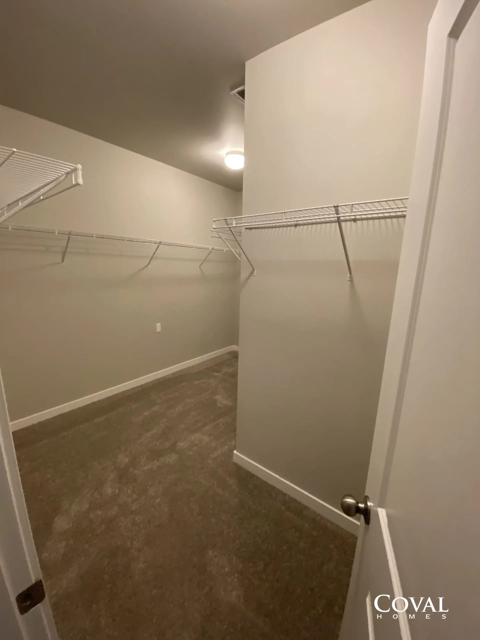 Empty walk-in closet with beige walls, white wire shelving, and carpeted floor.