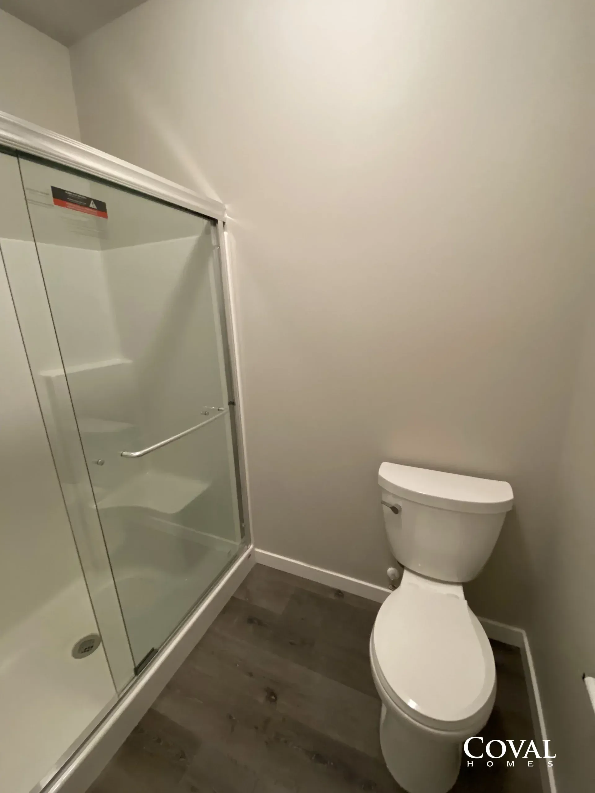 Small bathroom with a glass shower enclosure and a white toilet on gray tile flooring.
