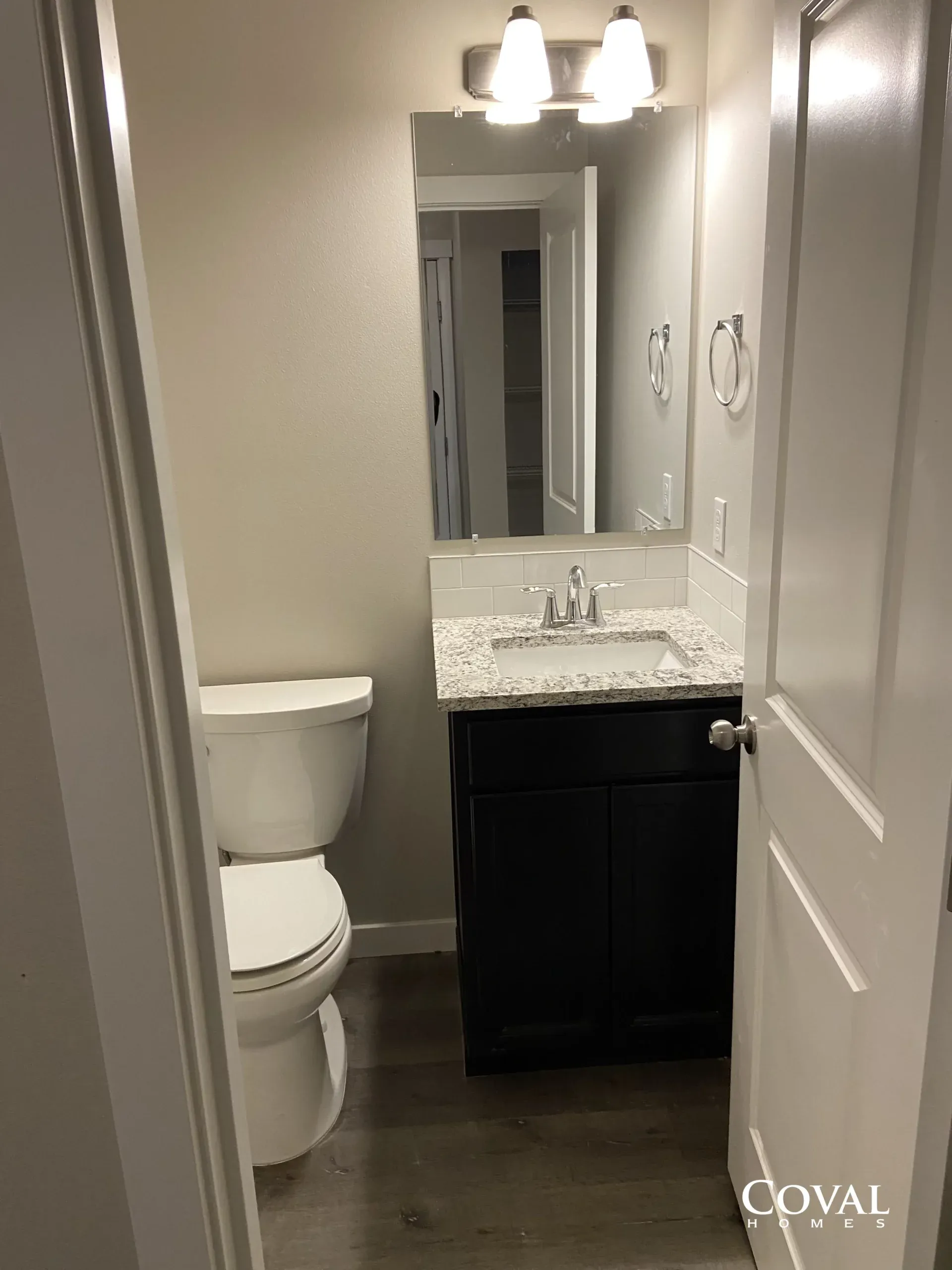 Small bathroom with toilet, dark vanity, granite sink, mirror, and wall lights.