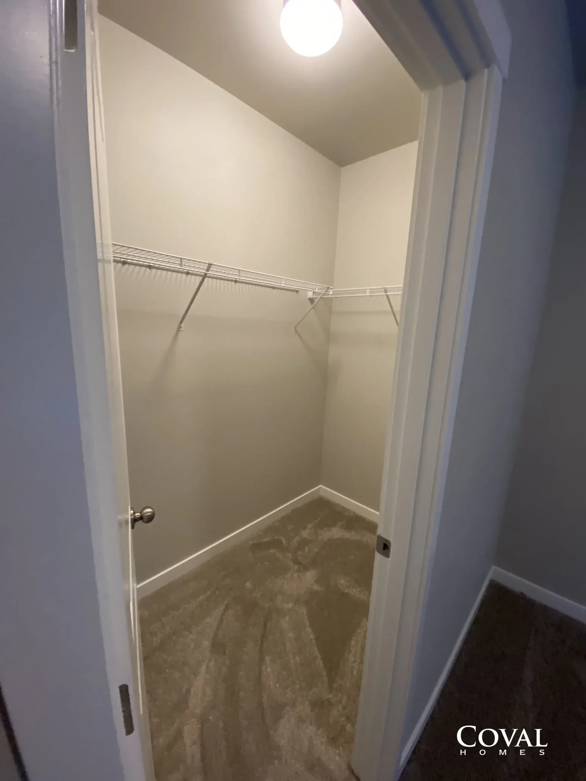 Empty walk-in closet with beige walls, white wire shelving, and wood-look flooring.