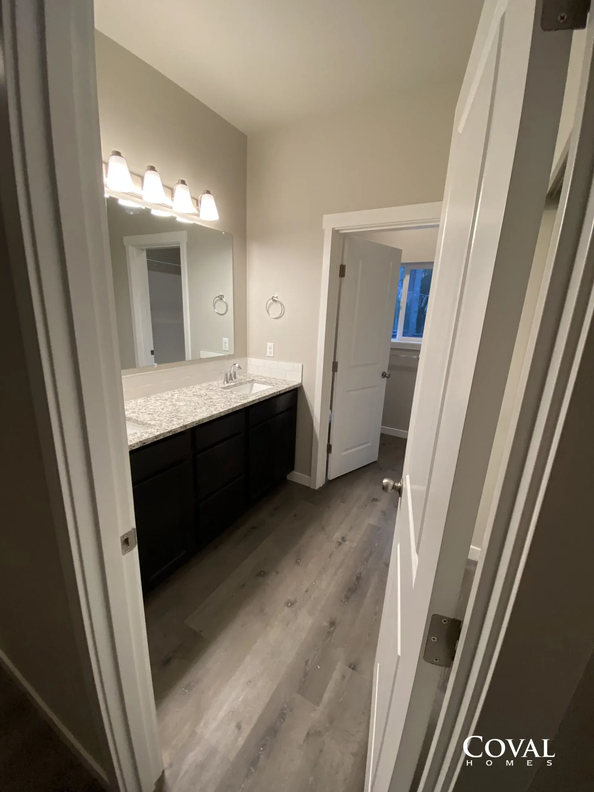 Bathroom vanity with large mirror, white countertops, dark cabinets, and wood-look flooring in a hallway view