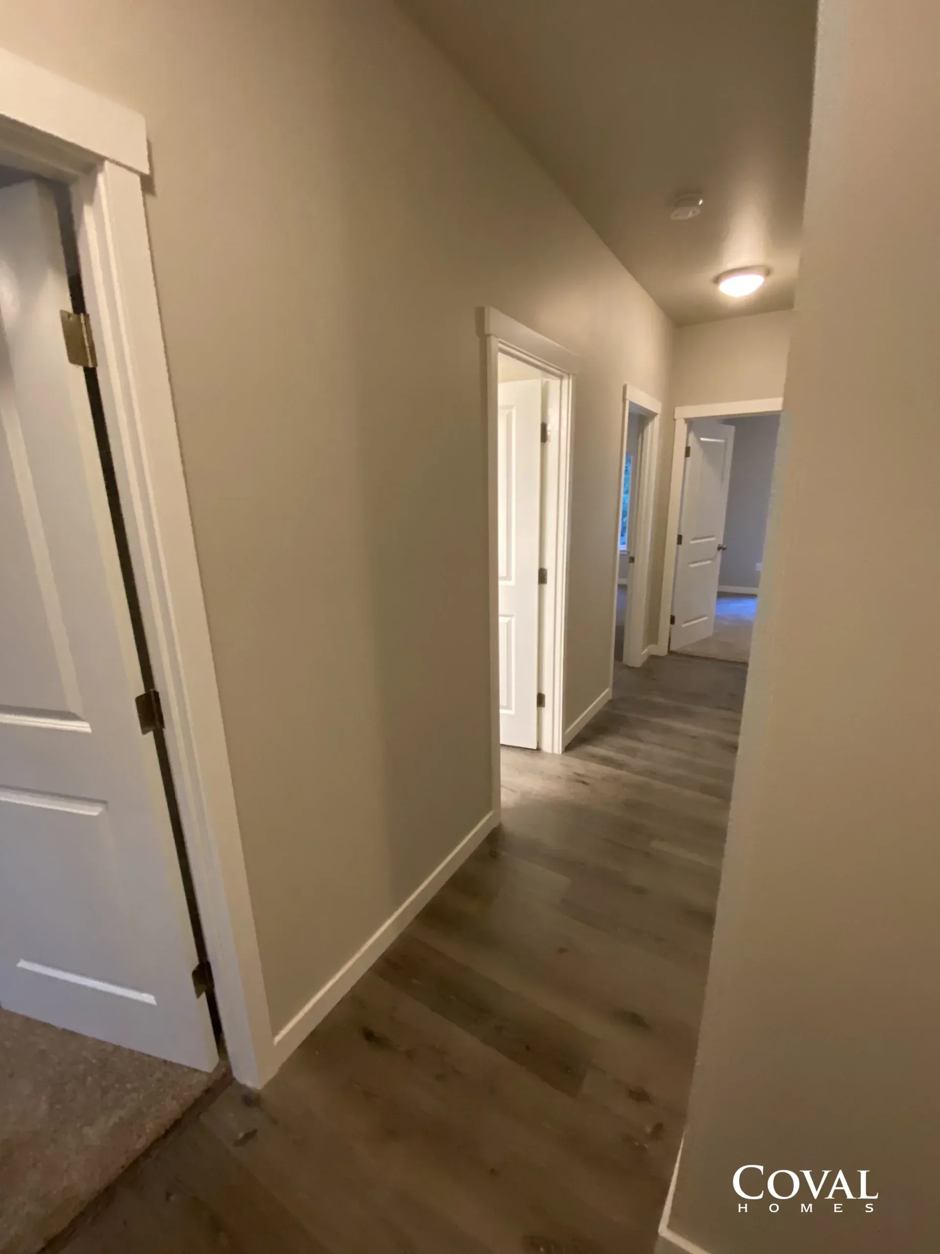 Narrow hallway with beige walls, white doors, and gray wood flooring in a home