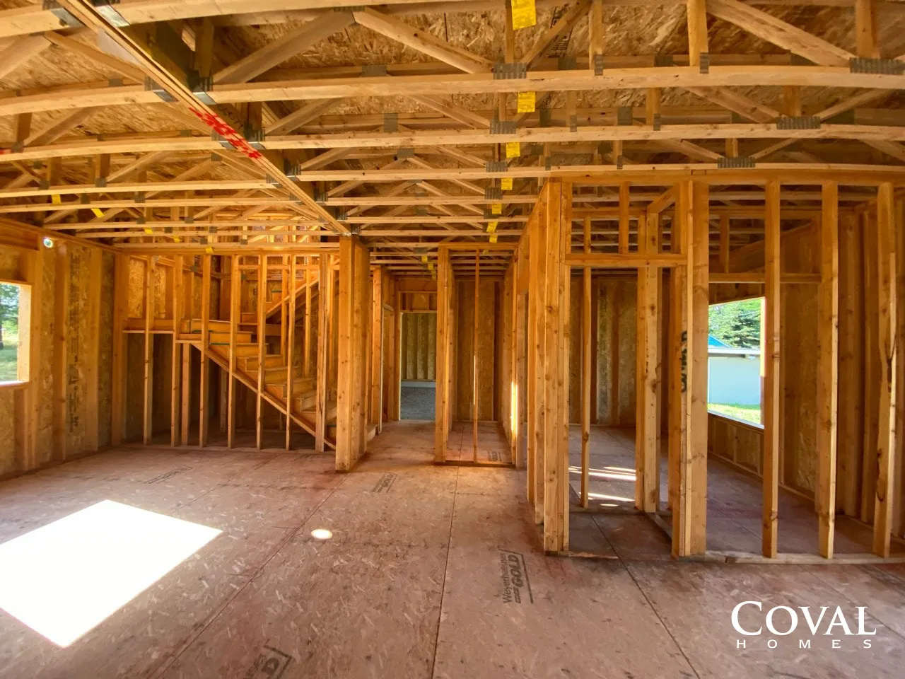 Unfinished house interior with exposed wooden framing and sunlight on plywood floor