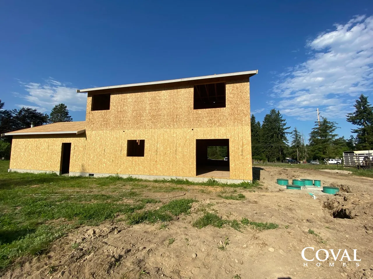 Two-story unfinished yellow house under construction on a dirt lot with blue sky overhead