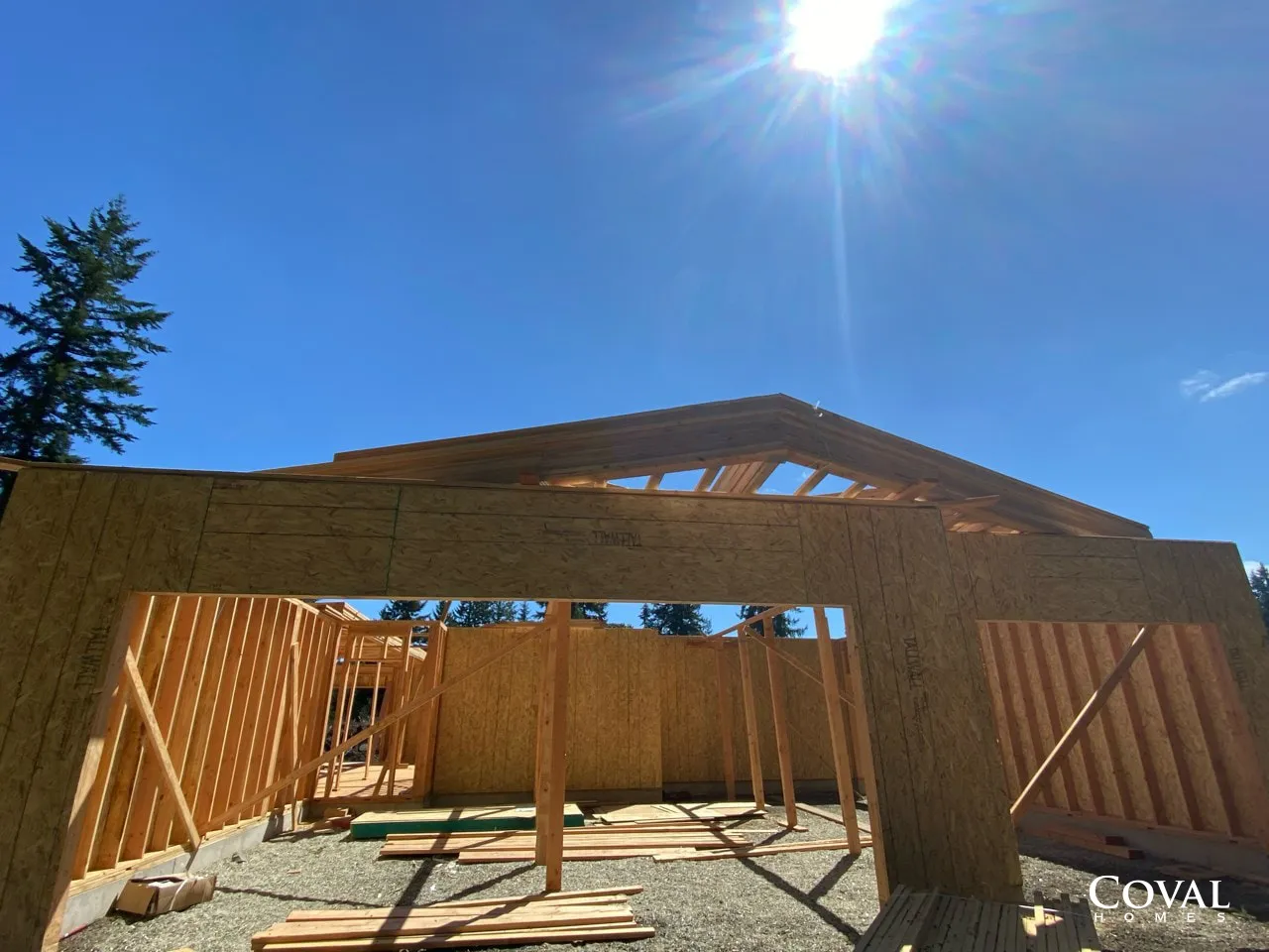 Wood-framed house under construction on a sunny day with blue sky and exposed roof trusses