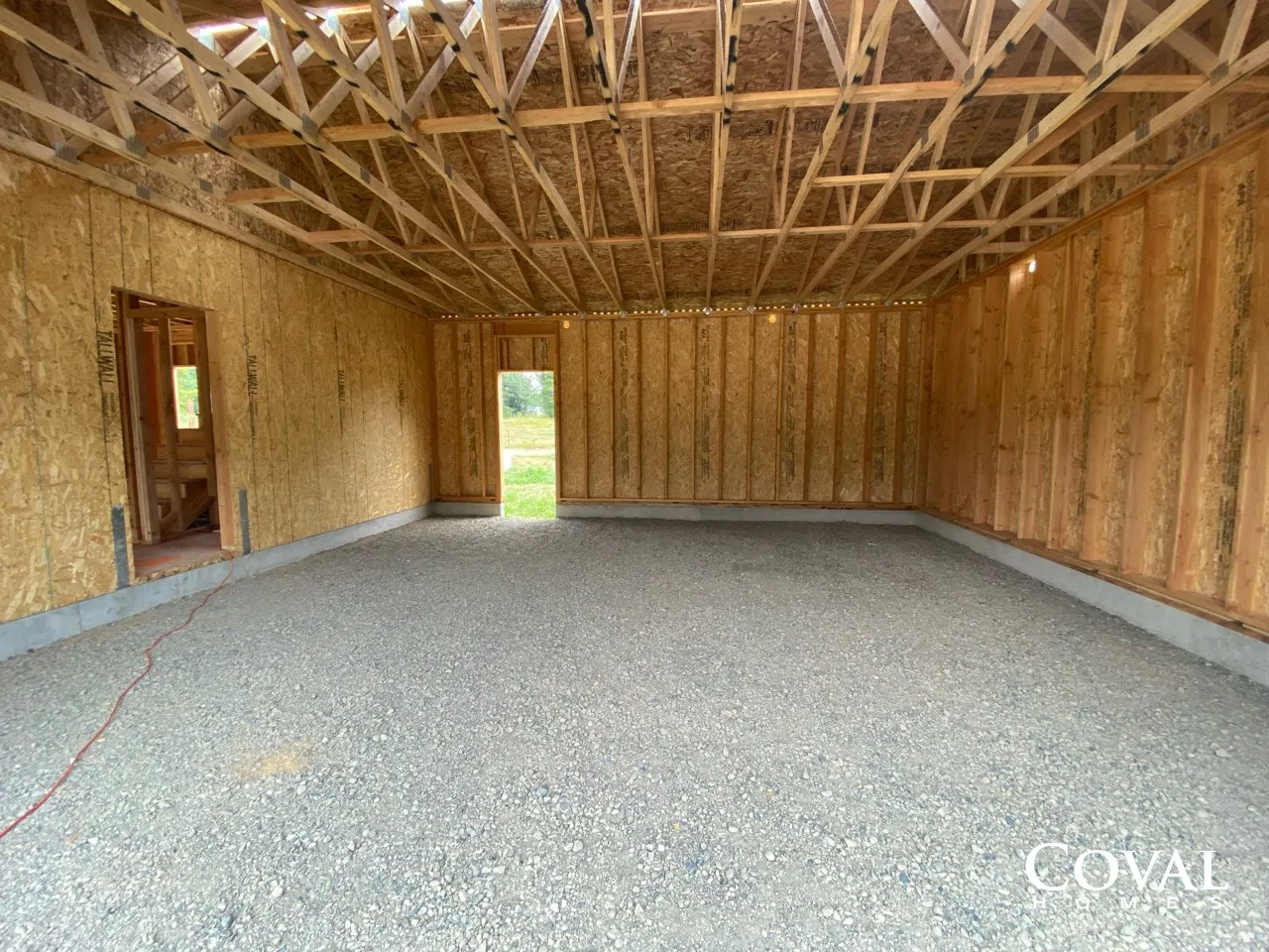 Empty framed garage interior with exposed trusses, wood studs, and gravel floor.