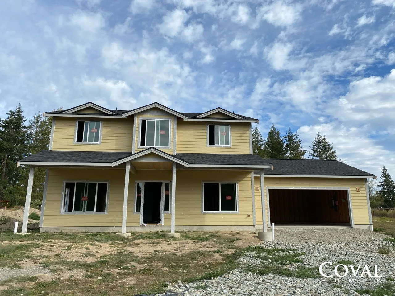 Two-story yellow house under construction with unfinished front porch and attached garage beneath a blue sky