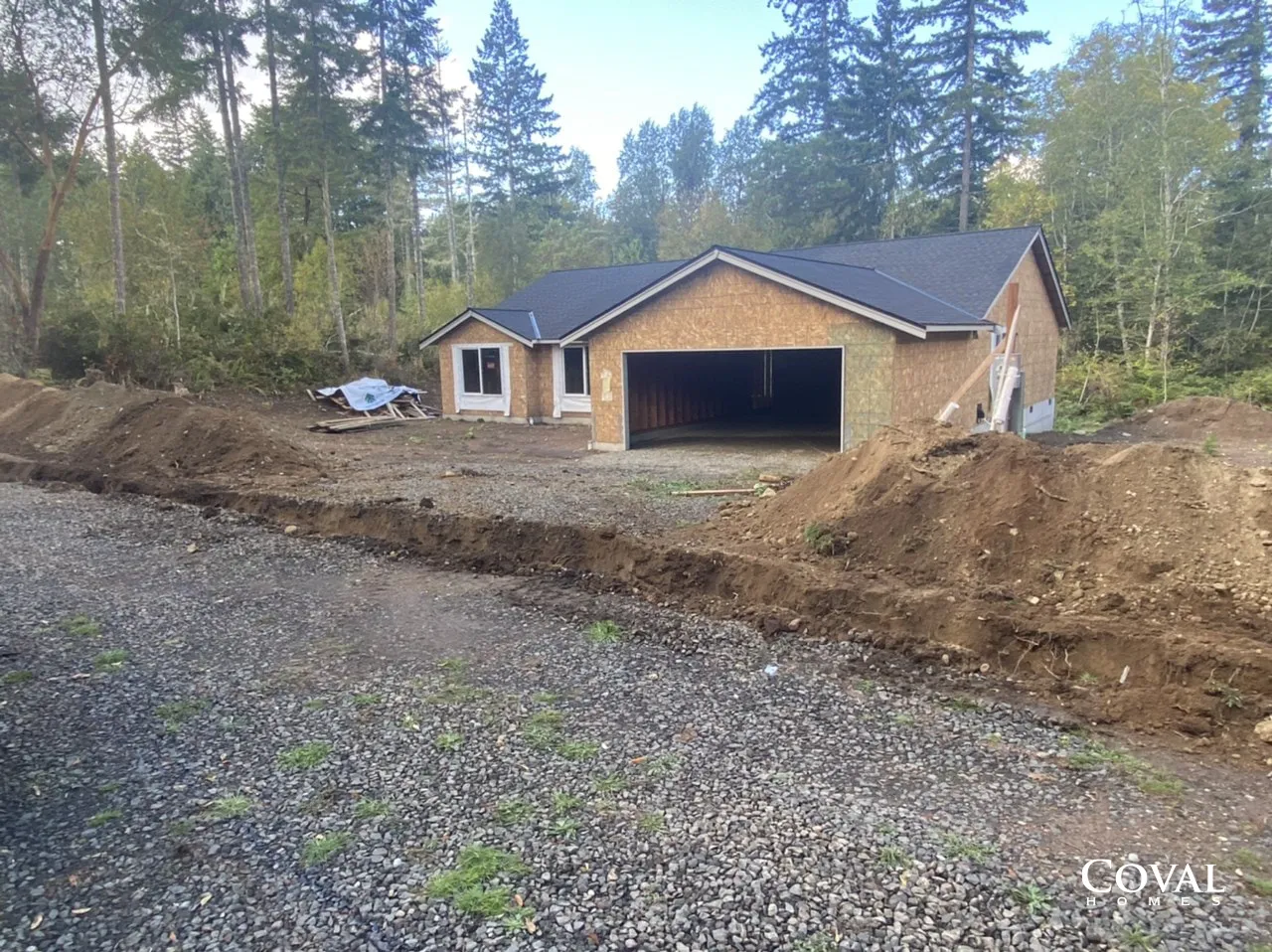 New house under construction beside a gravel driveway in a wooded area