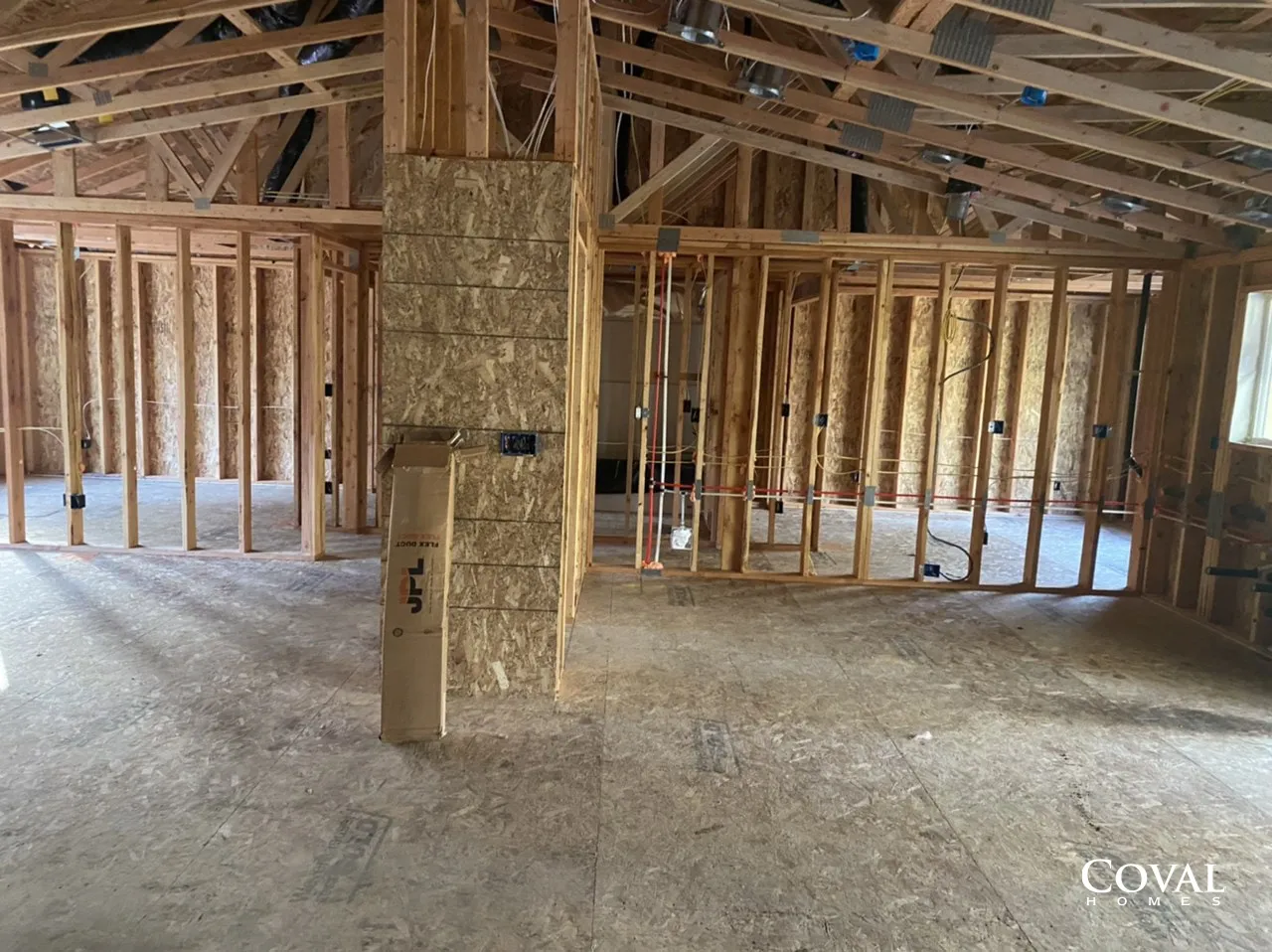 Unfinished house interior with exposed wooden framing, roof trusses, and a central stone chimney.
