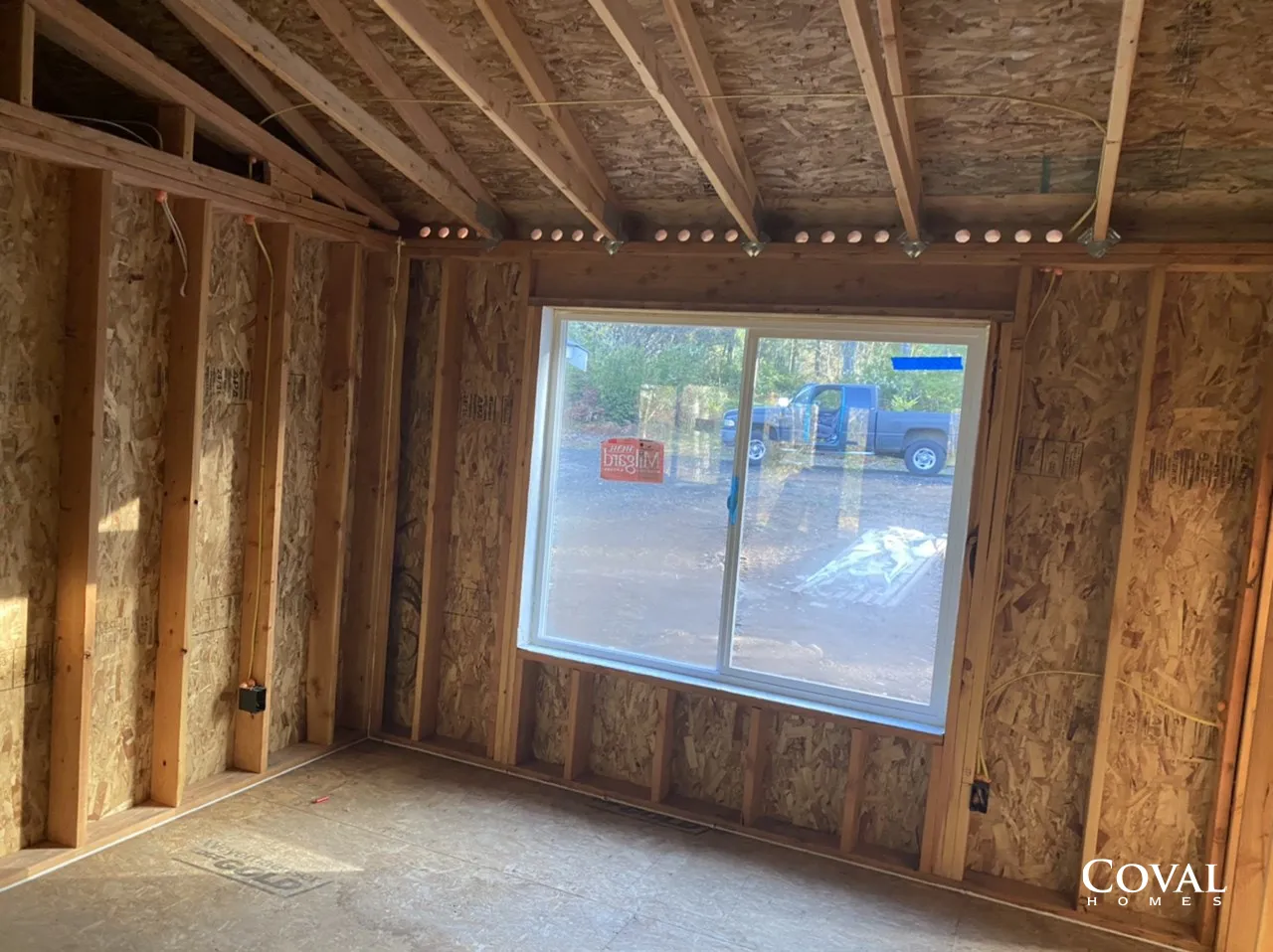 Interior of an unfinished wood-framed room with a large window and exposed studs.