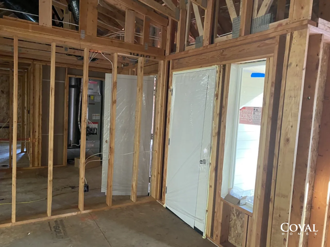 Interior of an unfinished house with exposed wooden framing and a doorway opening to daylight.