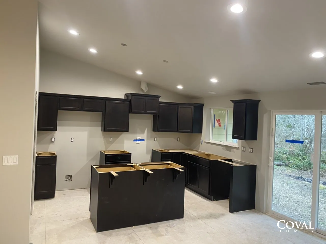 Modern kitchen with black cabinets, central island, and sliding door to a backyard